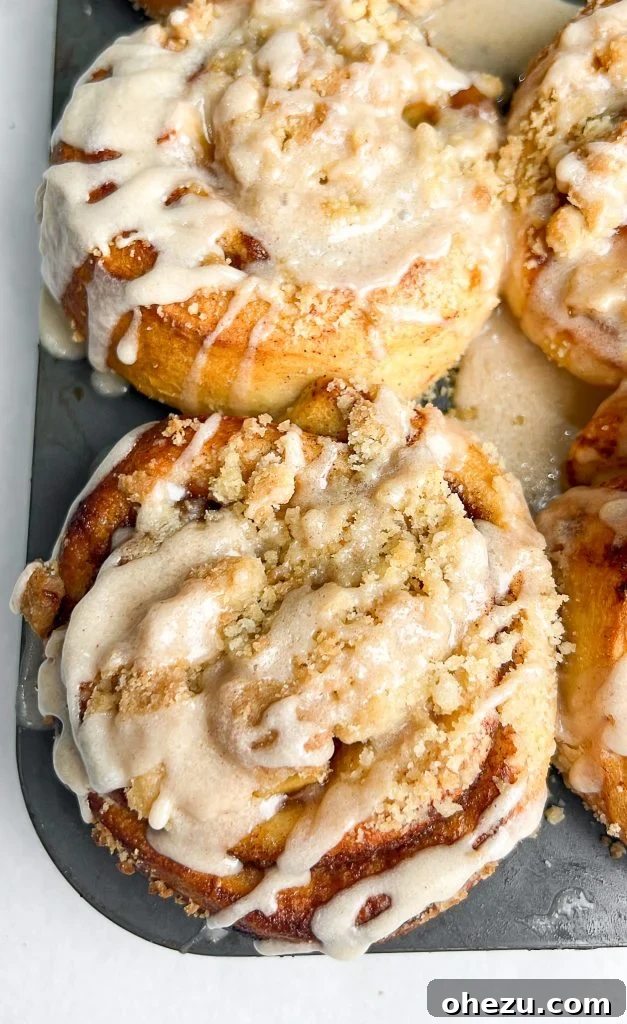 A tray of freshly baked apple pie cinnamon rolls, with some already drizzled with icing
