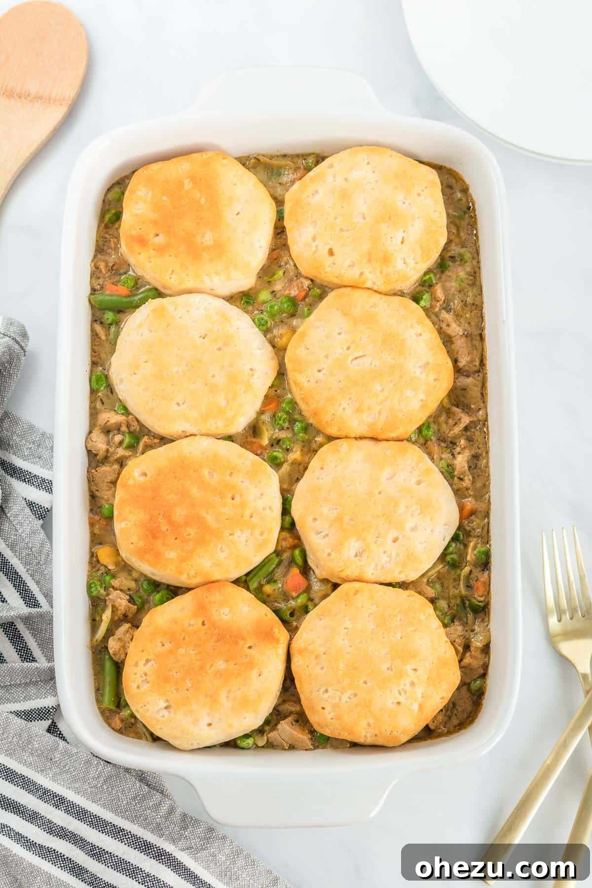 Hearty vegetarian pot pie filling in a rustic casserole dish, generously topped with golden, flaky biscuits, ready to be served as a comforting meal.