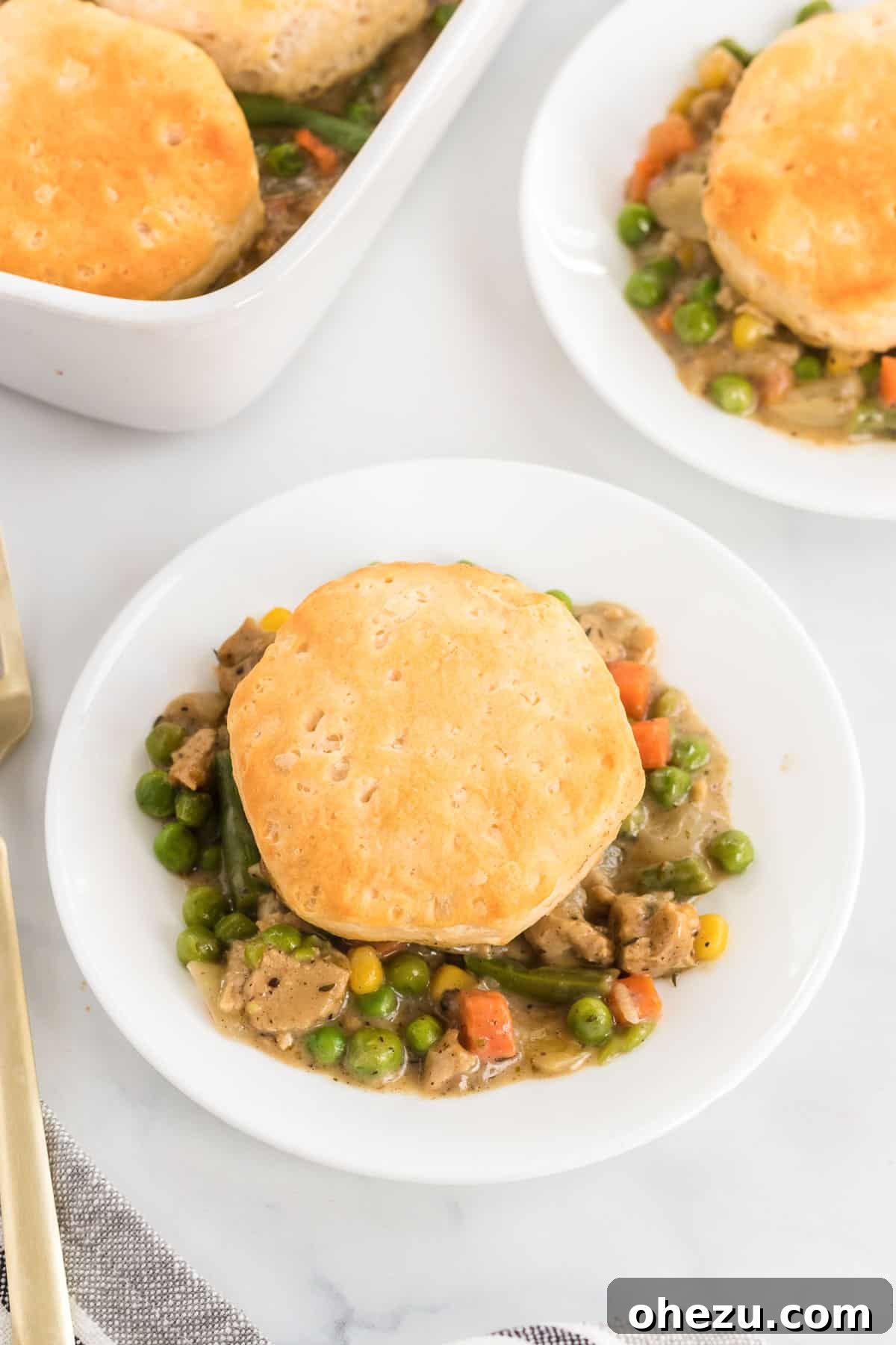 A close-up of a single serving of deconstructed veggie pot pie, with a golden biscuit resting atop the creamy vegetable filling in a white bowl.