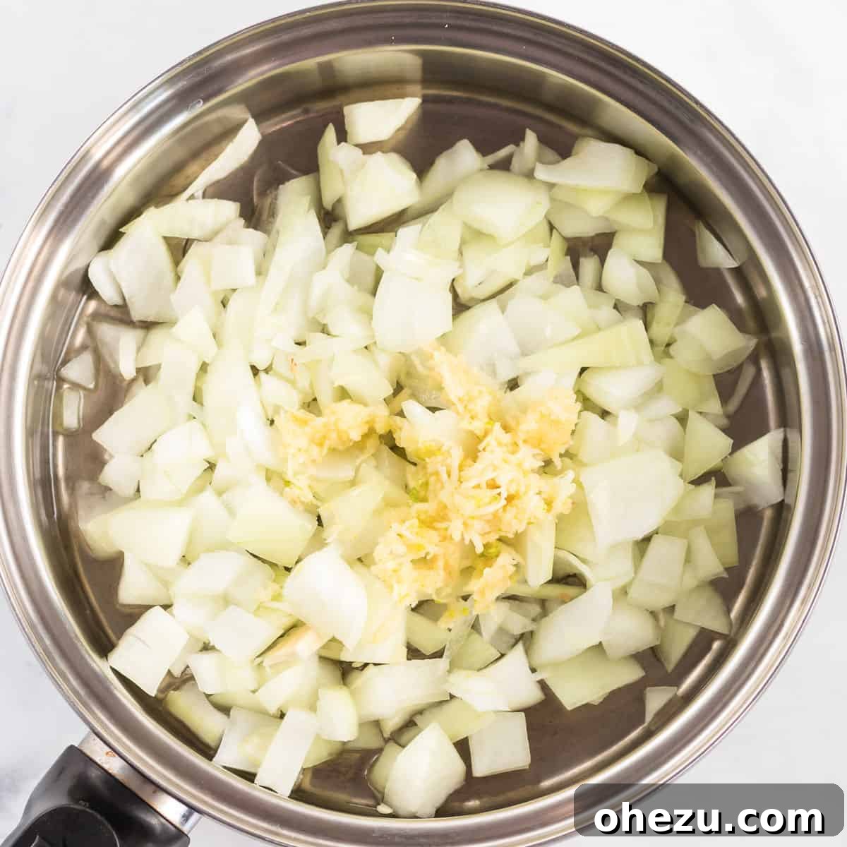 Freshly diced onion and minced garlic sizzling in olive oil in a stainless steel sauce pan, starting the base for the veggie pot pie filling.