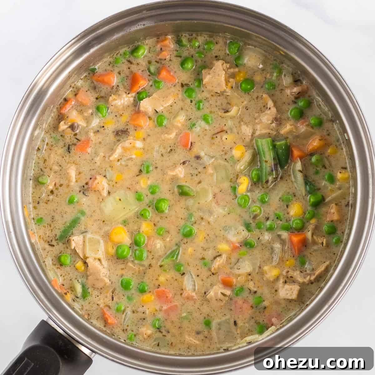 A rich and creamy vegetarian pot pie filling, generously seasoned and bubbling gently in a large sauce pan, ready for the oven.