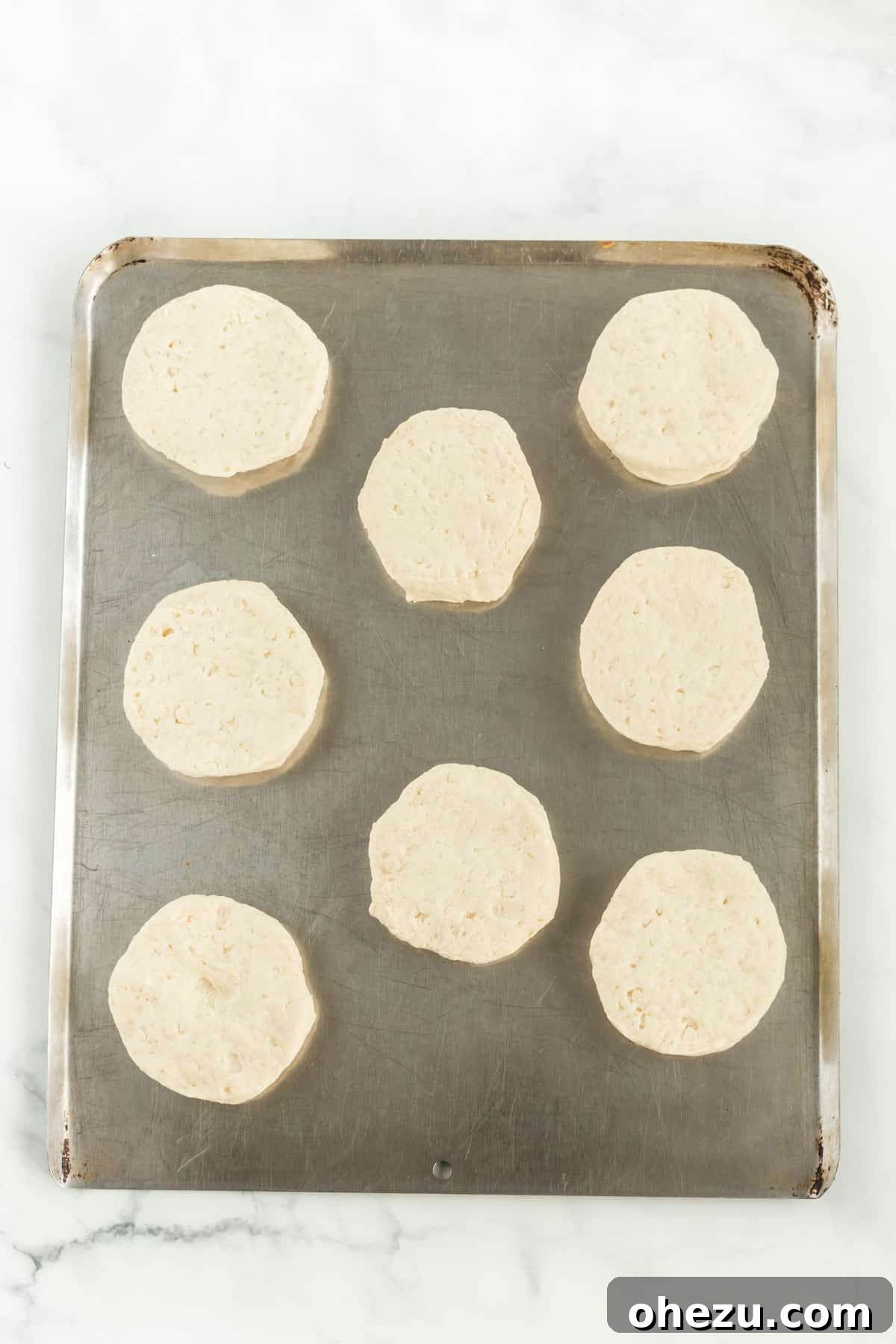 Raw, ready-to-bake biscuits neatly spaced on a non-stick cookie sheet, prepared for baking to a golden crisp.