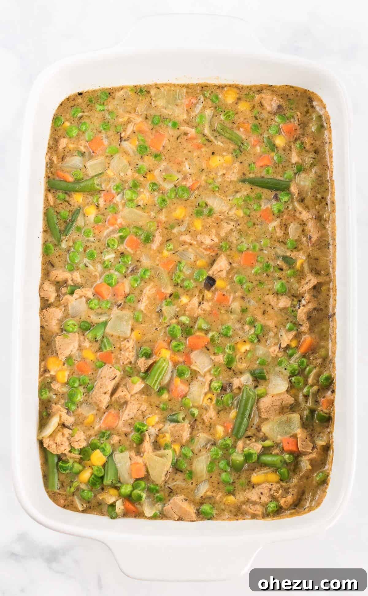 Creamy vegetarian pot pie filling, bubbling hot in a glass casserole dish, freshly transferred and ready to be baked in the oven.