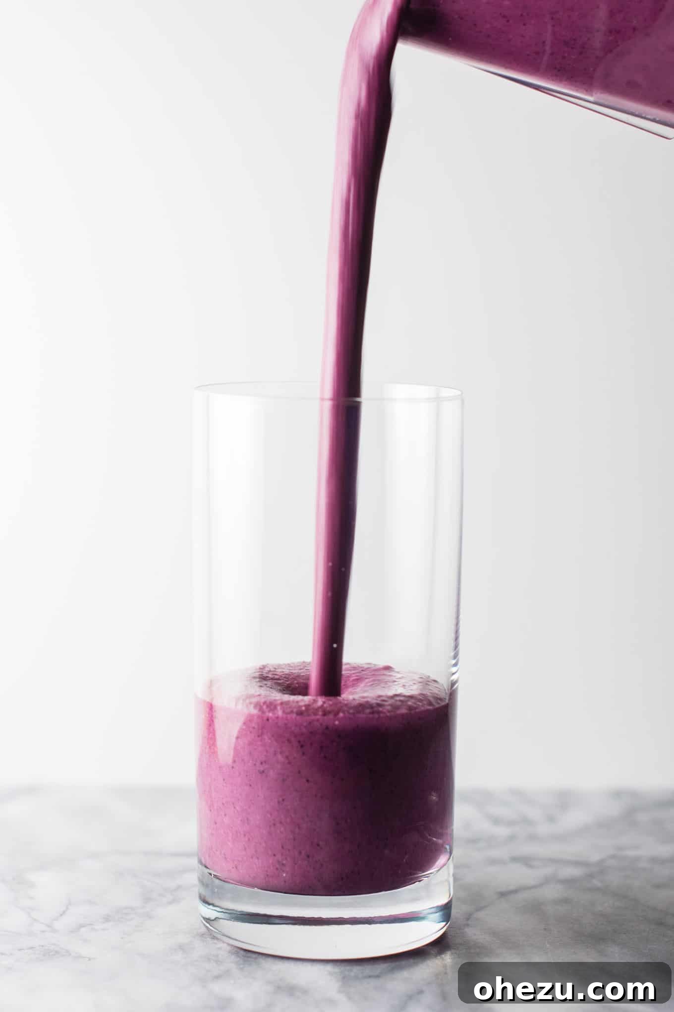 A glass of homemade blueberry pie smoothie positioned next to a small bowl of fresh blueberries and lemon, showcasing the fresh ingredients used in the recipe. #healthy #blueberrysmoothie #blueberrypiesmoothie #vegetarian #greekyogurt #lemonzest #glutenfree