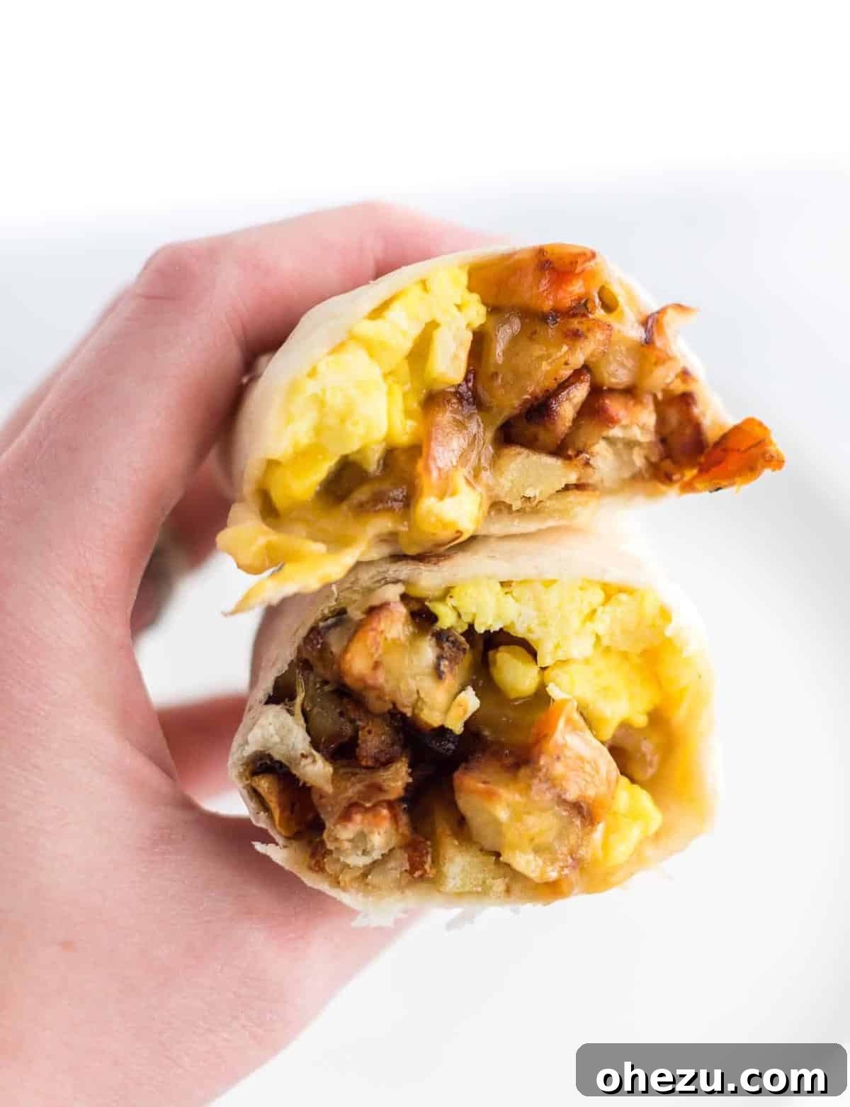 Breakfast Burrito Bliss 2 A hand holding a perfectly cut breakfast burrito, revealing layers of fluffy eggs, crispy hash, and melted cheddar cheese.