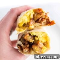 A hand holding a breakfast burrito cut open, revealing its rich fillings.