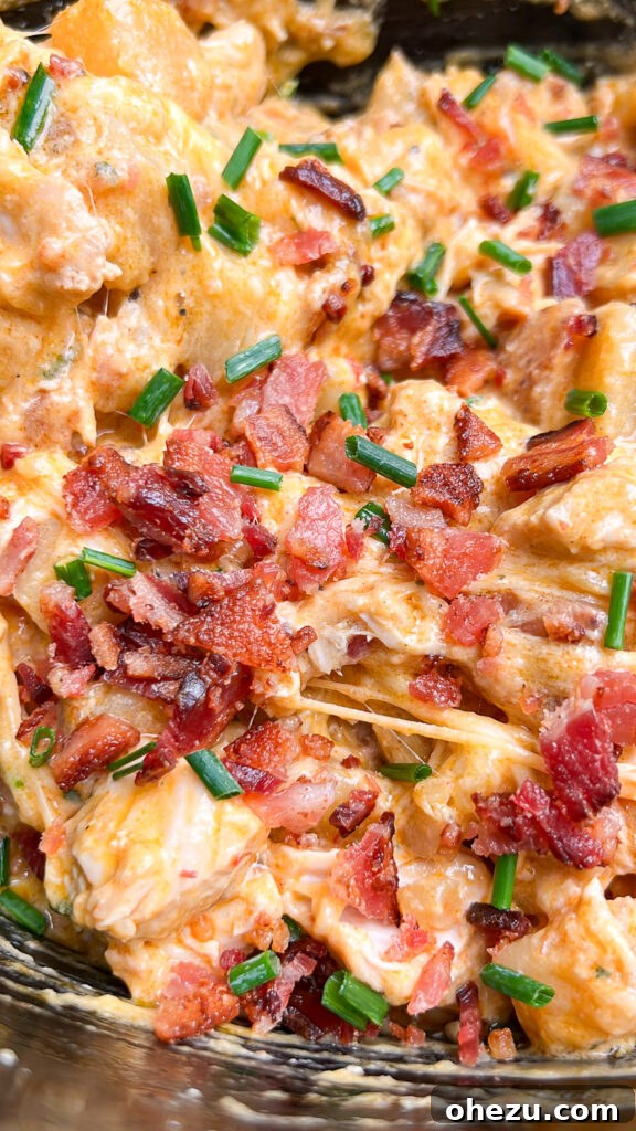 Loaded Slow Cooker Ranch Chicken and Potatoes 4 Overhead view of a slow cooker filled with Cheesy Bacon Ranch Chicken and Potatoes, topped with melted cheese and fresh chives.