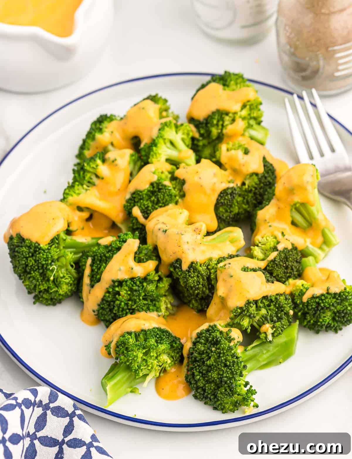 Creamy cheddar cheese sauce drizzled over fresh steamed broccoli florets in a bowl.