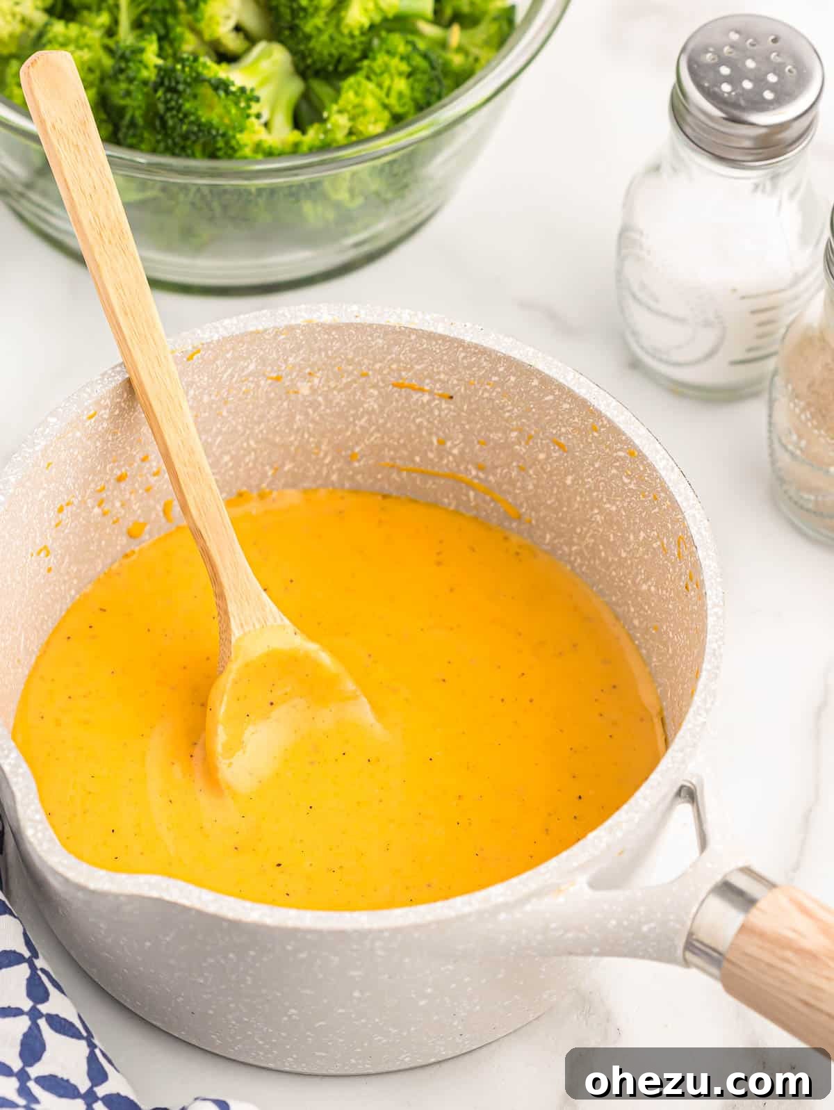 A close-up of a saucepan with rich, smooth cheddar cheese sauce, ready for serving or storage.