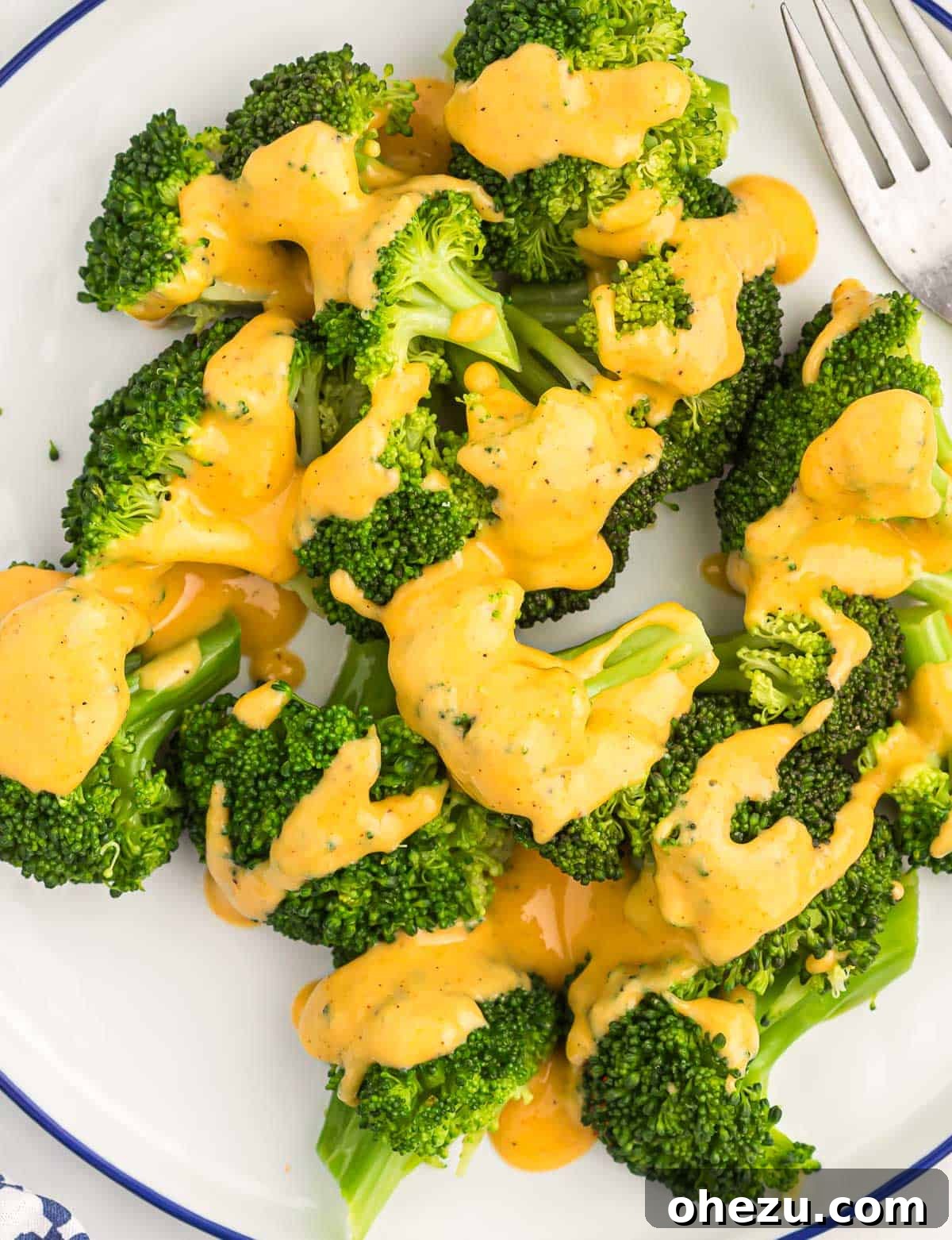 A vibrant green pile of steamed broccoli florets beautifully drizzled with creamy, golden cheese sauce, ready to be served.