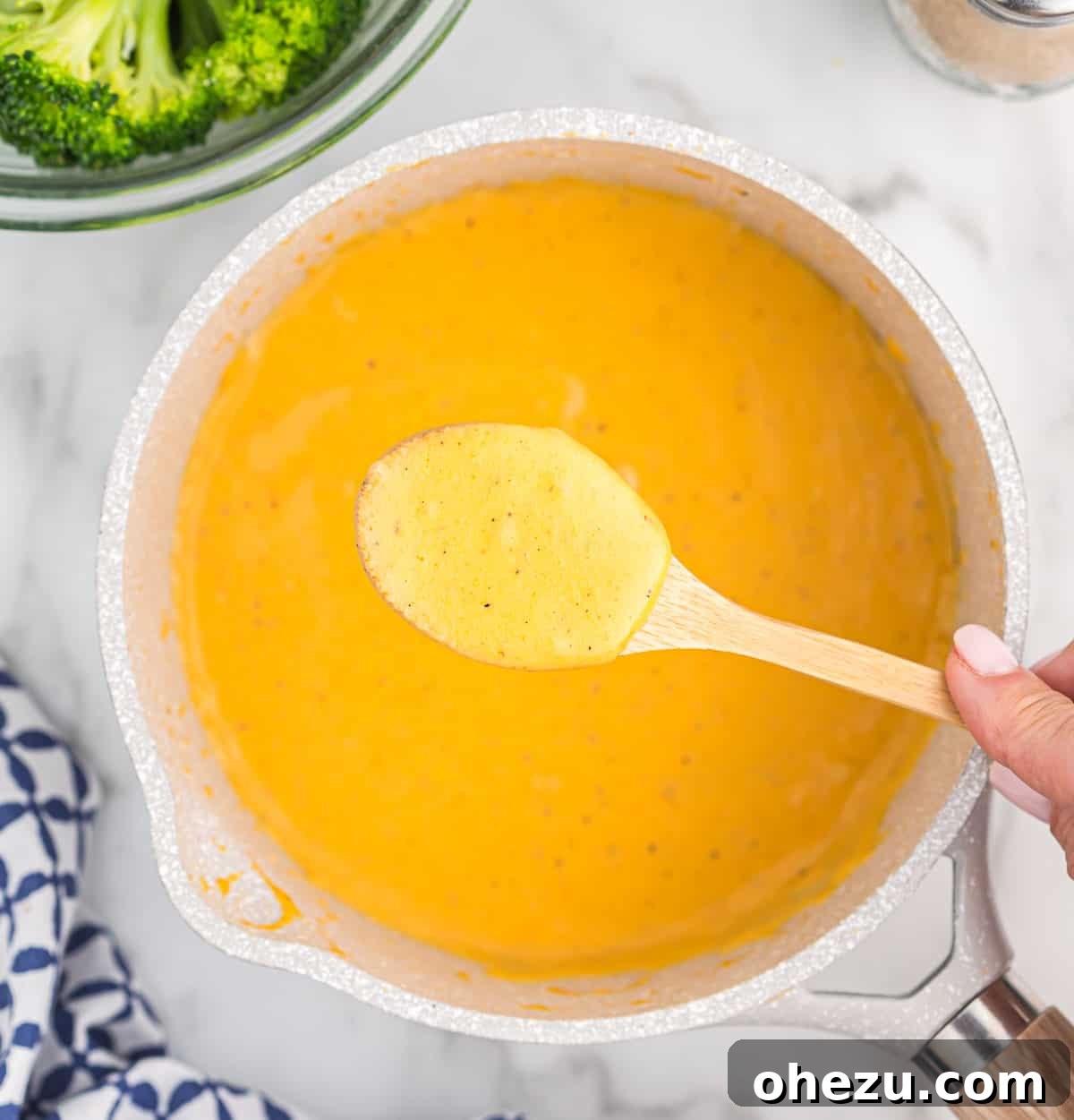 A wide shot of a saucepan filled with golden cheddar cheese sauce, showing its smooth and thick consistency, ready to be poured.