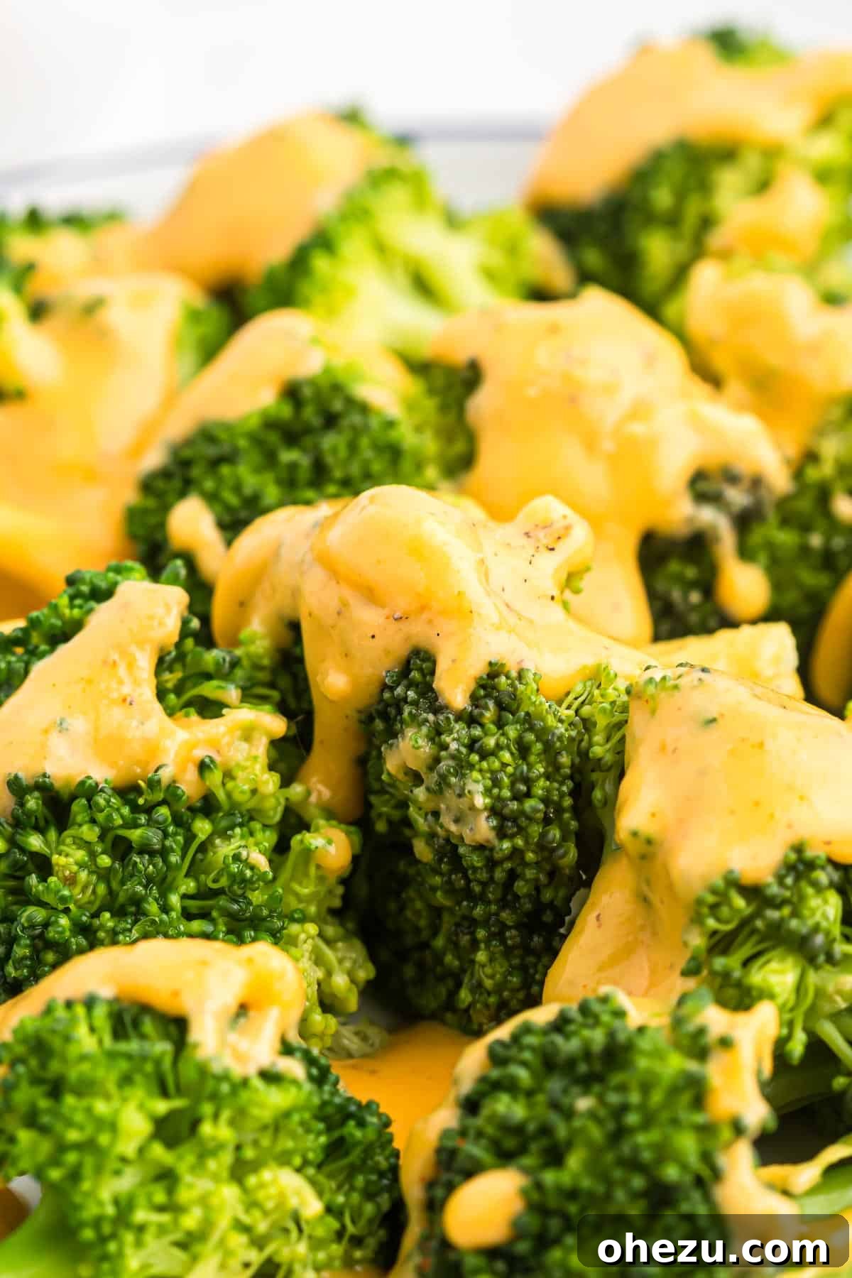 A bowl of vibrant green steamed broccoli florets generously topped with a rich, golden cheddar cheese sauce, ready to be enjoyed.