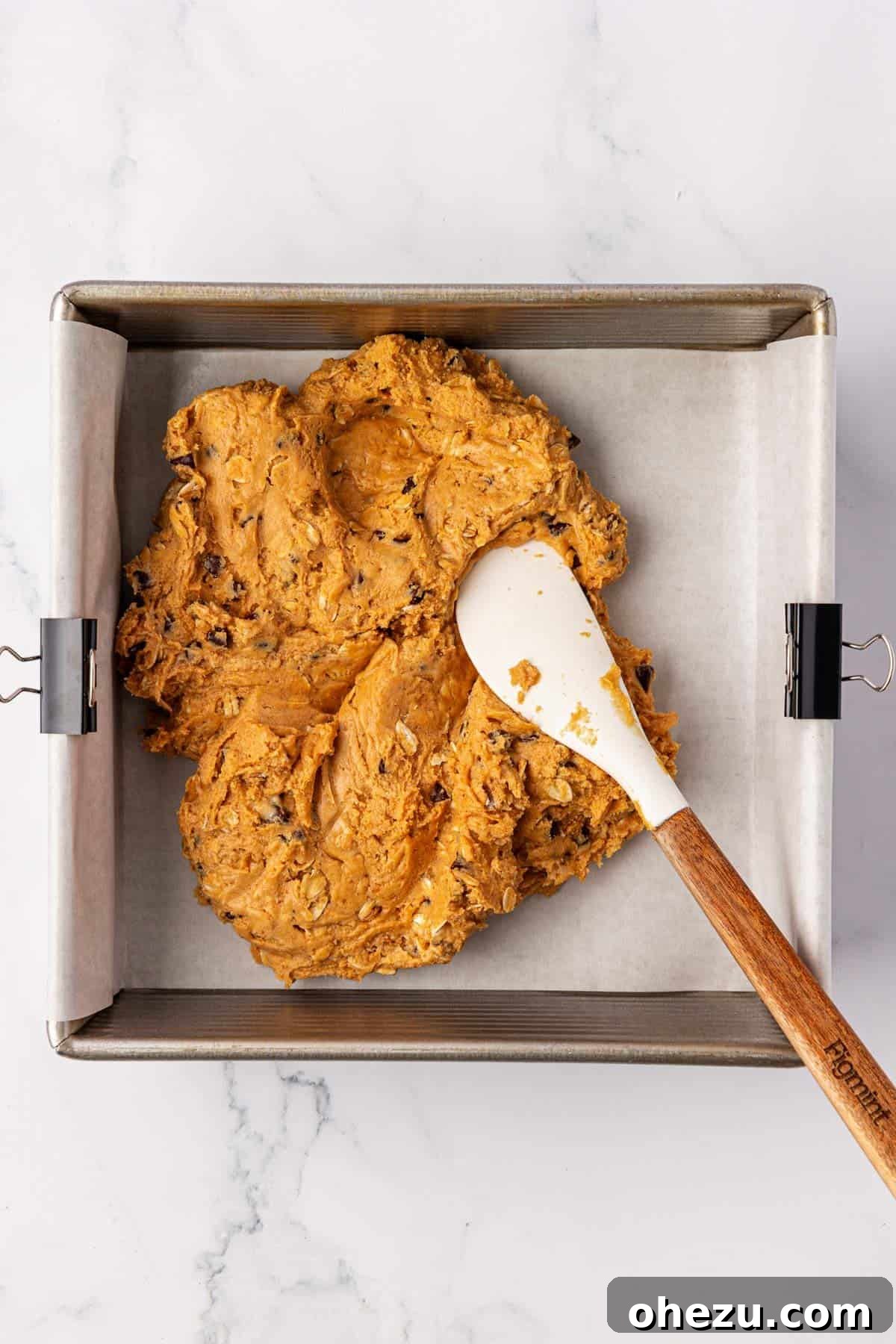 Pressing the protein bar batter into an 8x8 baking dish lined with parchment paper