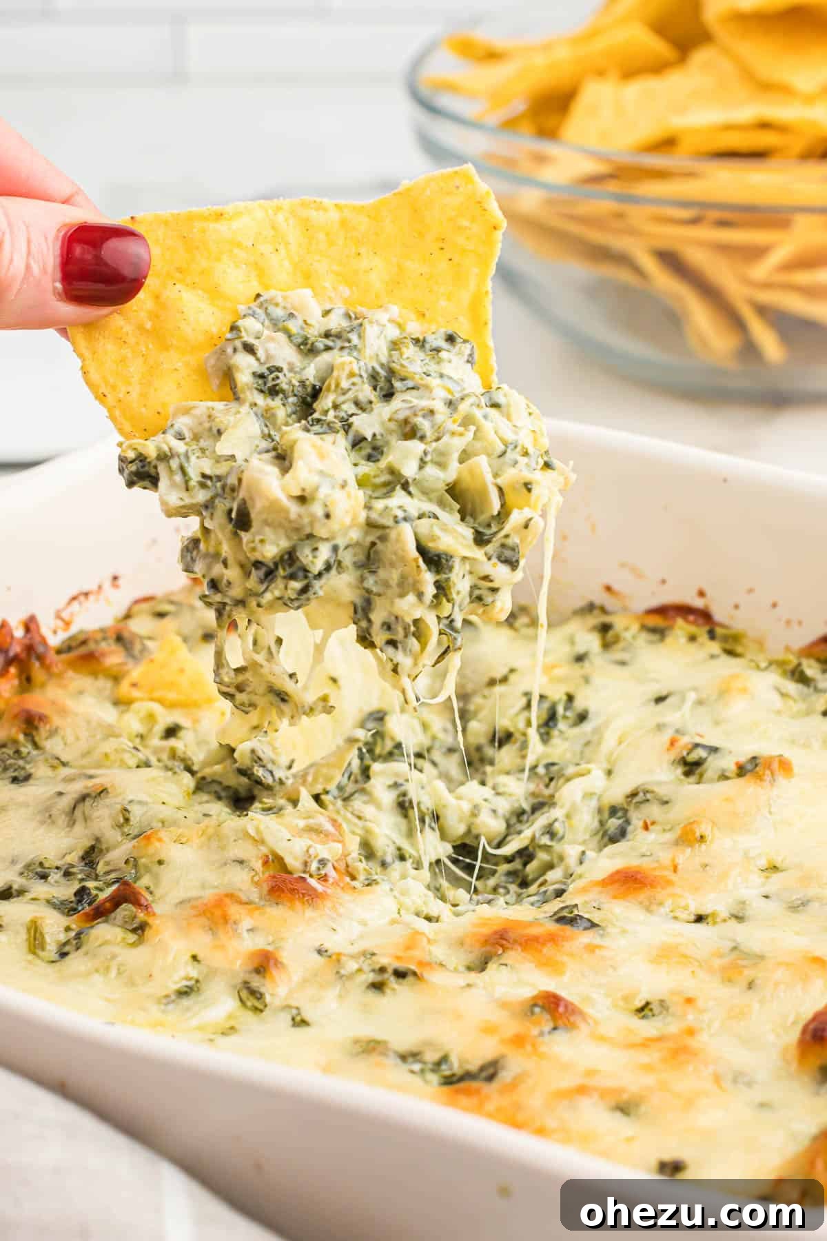 A close-up of another tortilla chip generously loaded with warm baked spinach artichoke dip, ready to be enjoyed.