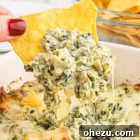 A delicious tortilla chip generously dipped into the ultimate baked spinach artichoke dip, highlighting its texture and warmth.