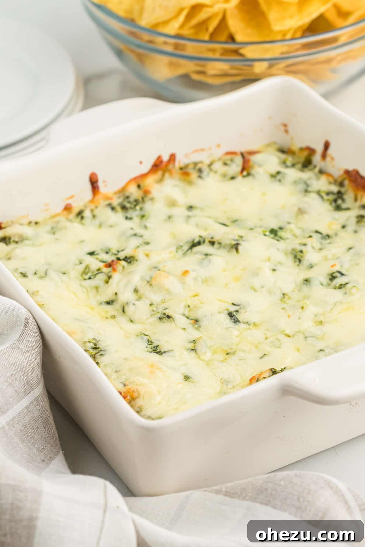 A close-up shot of hot, bubbly baked spinach artichoke dip in a white ceramic dish, garnished with a sprinkle of fresh parsley.