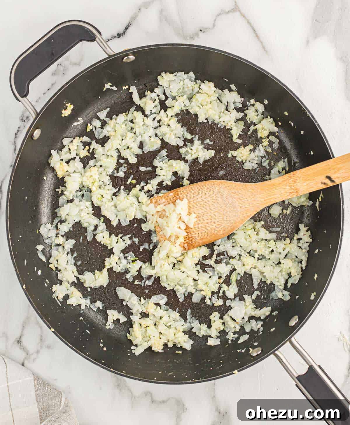 A close-up view of diced onions and minced garlic sizzling in olive oil within a hot skillet on a stovetop, browning beautifully.