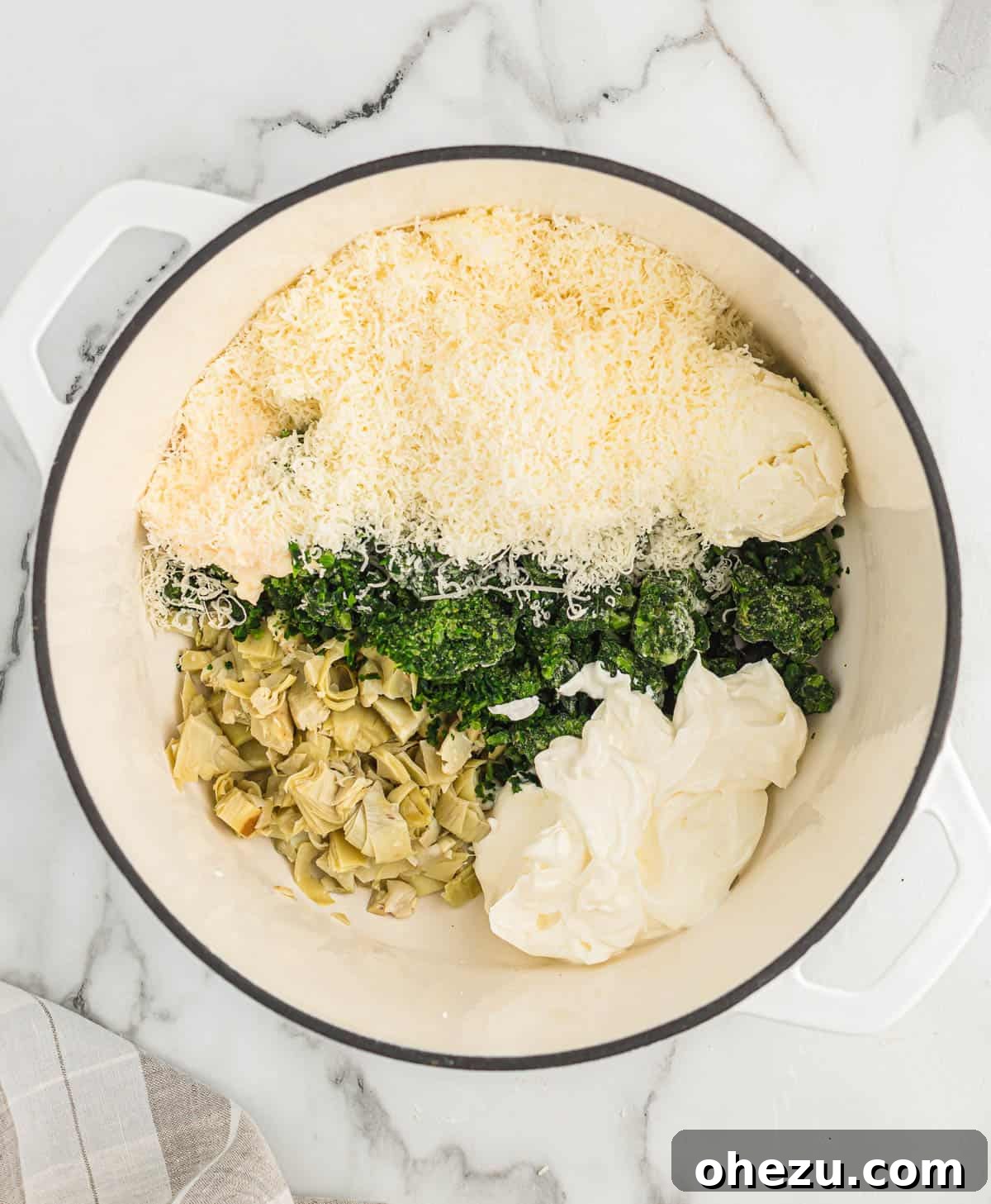 All the creamy dip ingredients, including spinach, artichokes, and cheeses, being added to a Dutch oven before heating.