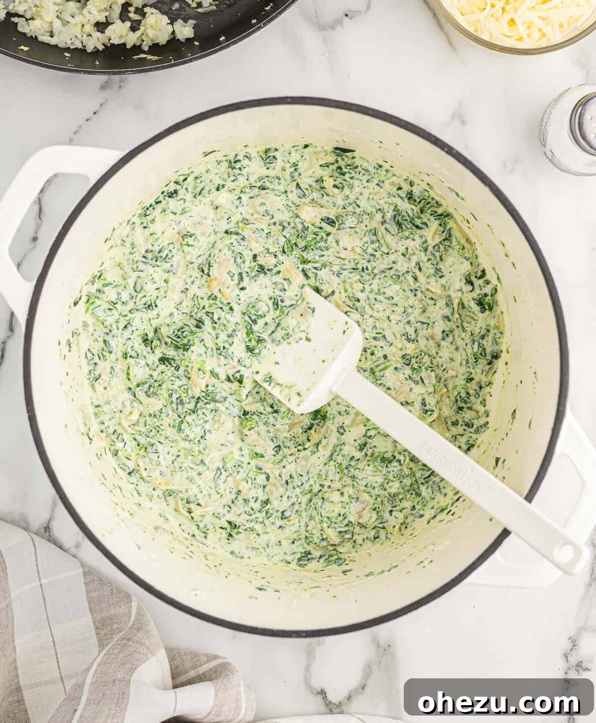 The spinach and artichoke dip mixture melting and combining in a Dutch oven over medium heat, becoming smooth and creamy.