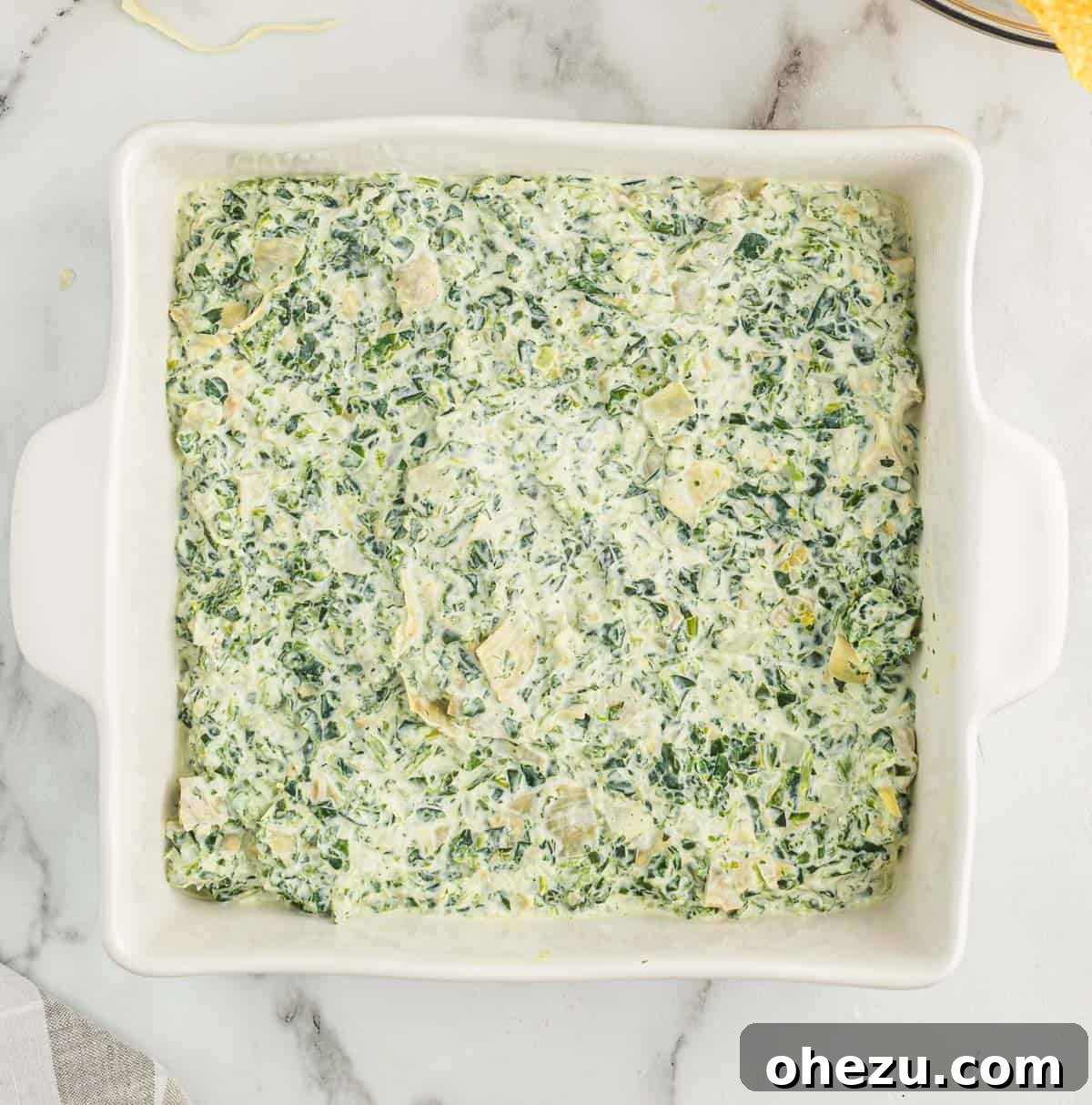 The prepared spinach artichoke dip mixture transferred into a clean white baking dish, ready for topping.