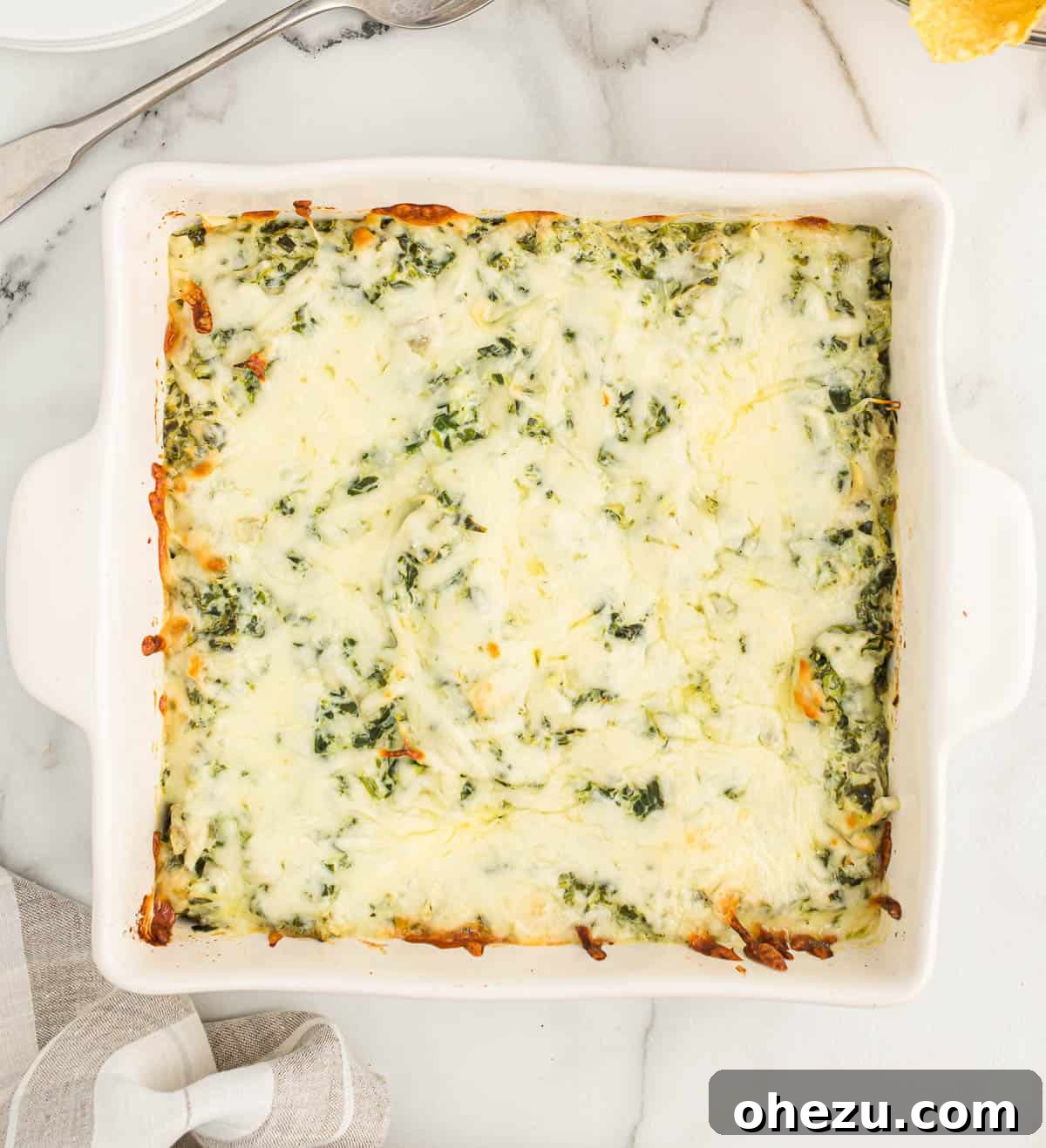 Freshly baked spinach artichoke dip served hot in a white ceramic dish, with a perfectly melted, golden-brown cheese crust.