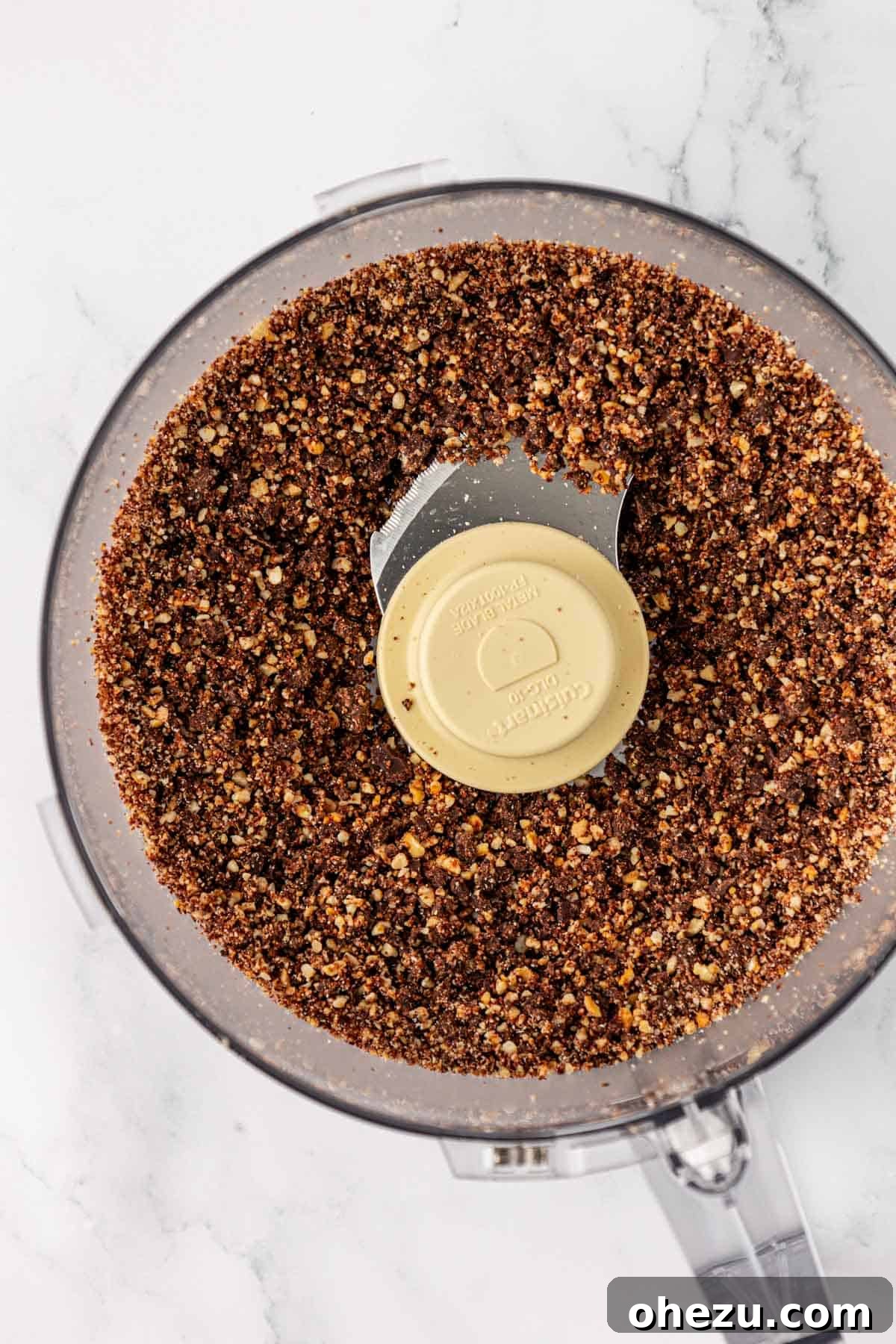 Food processor contents showing pulsed dark chocolate chips and cashews in small pieces