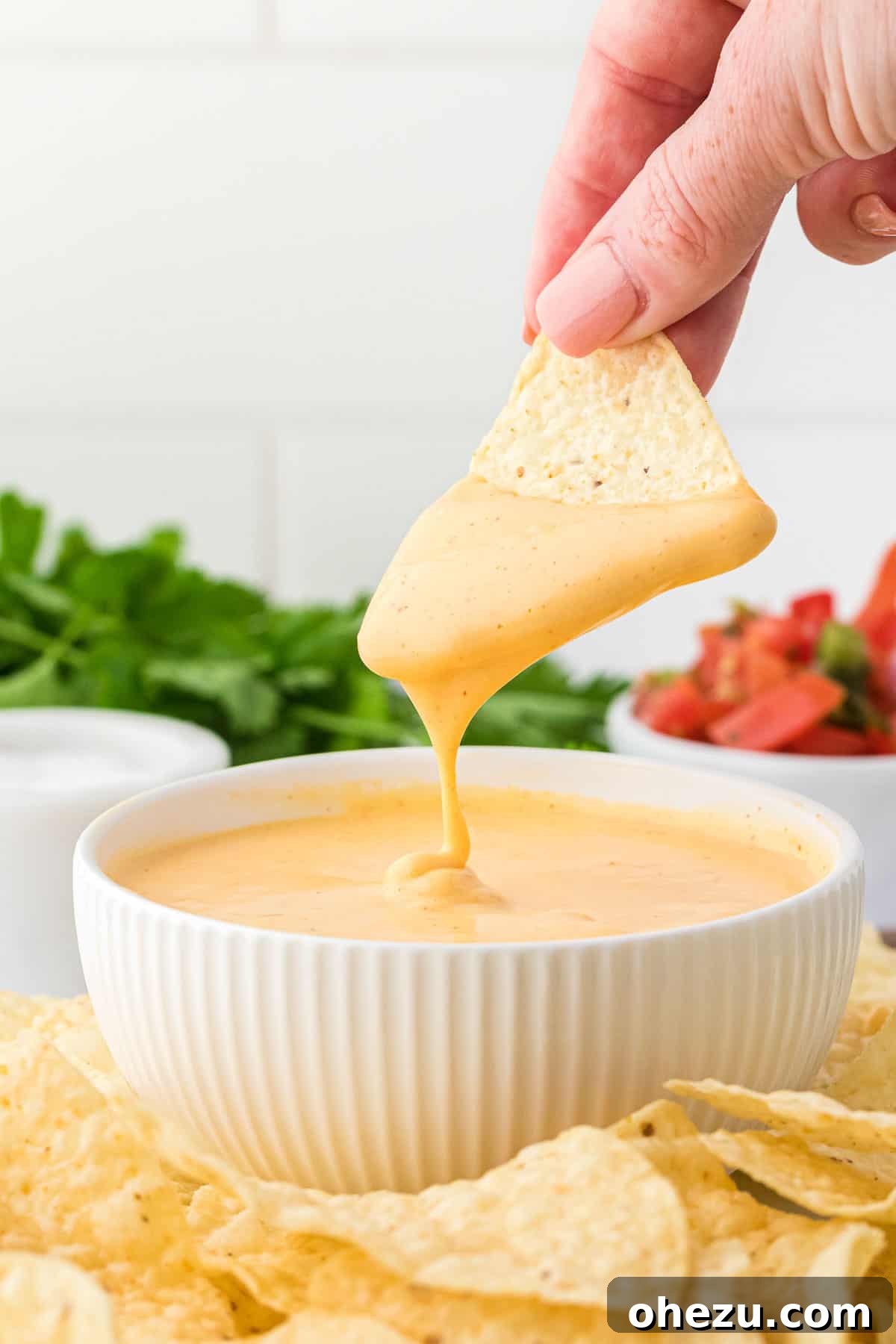 A chip being dipped into a bowl of creamy, golden nacho cheese sauce, surrounded by more tortilla chips.