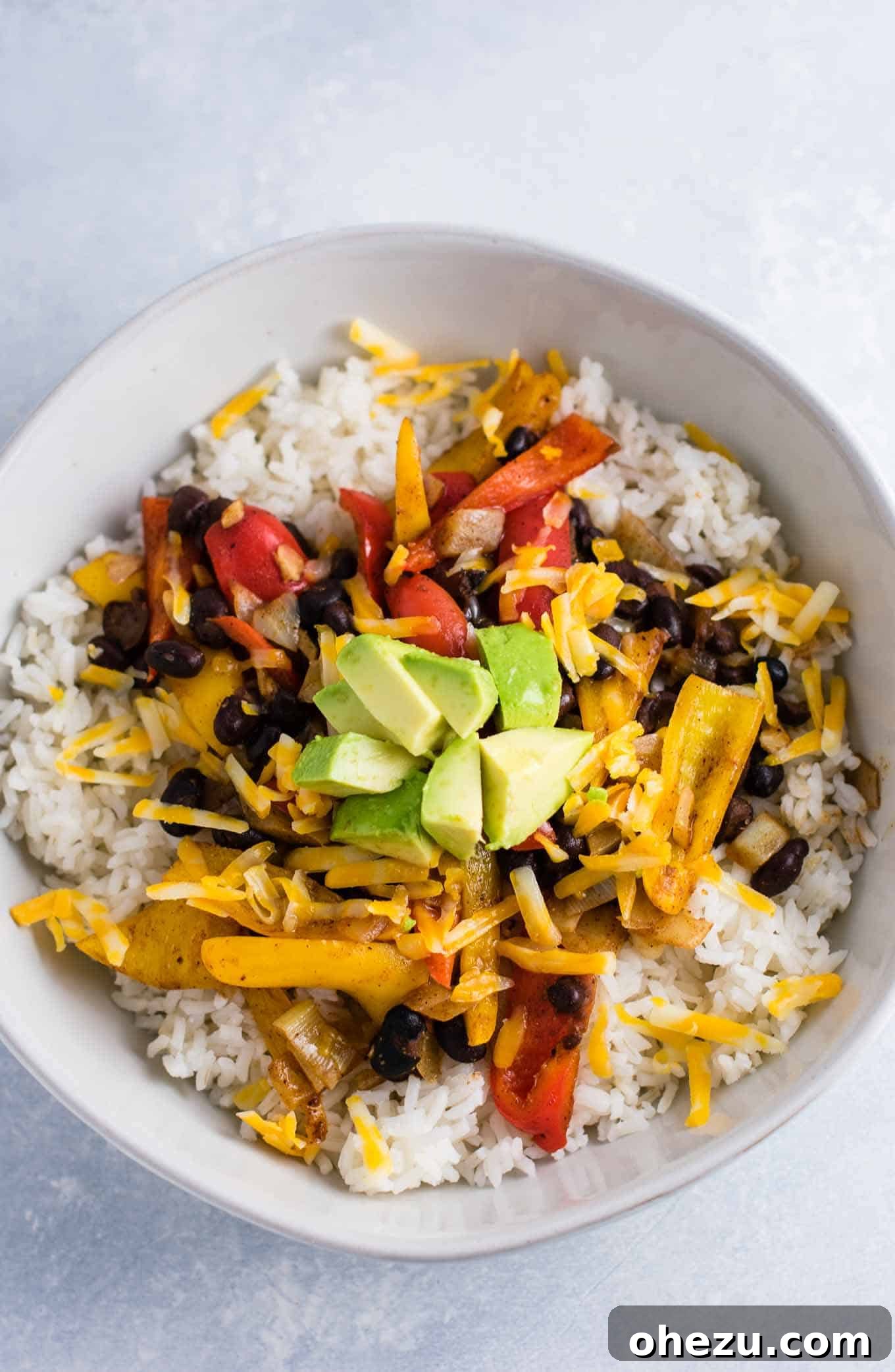 A vibrant Vegetarian Burrito Bowl, filled with black beans, corn, bell peppers, rice, and fresh avocado slices, presented in a white bowl.