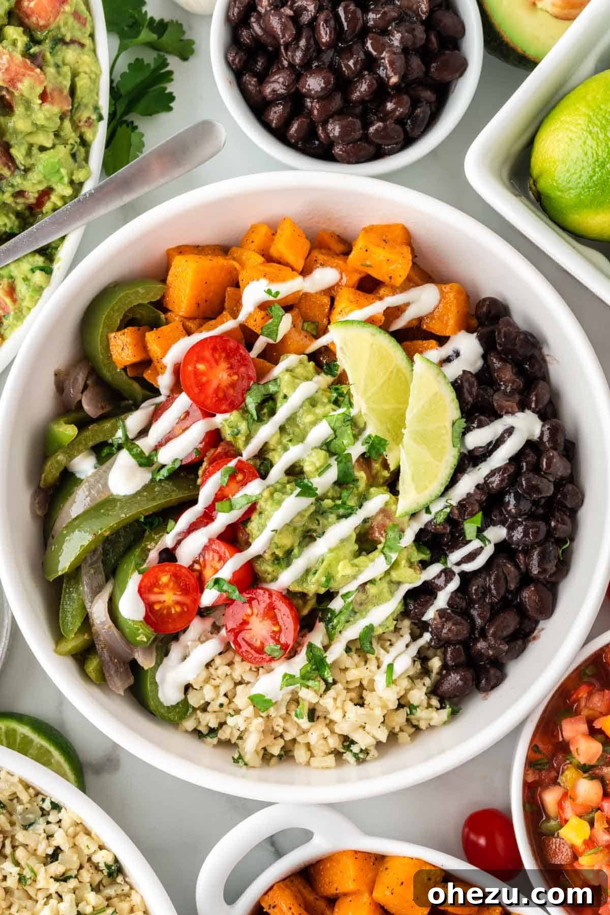 A colorful cauliflower rice burrito bowl, generously topped with black beans, fajita veggies, sweet potatoes, and a dollop of fresh guacamole.