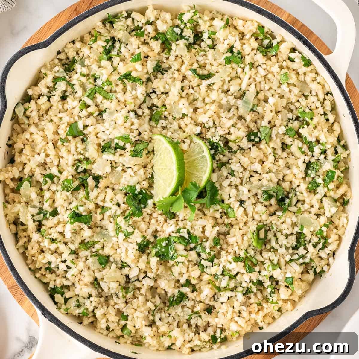 Cilantro Lime Cauliflower Rice cooked in a skillet, garnished with fresh cilantro and lime wedges.