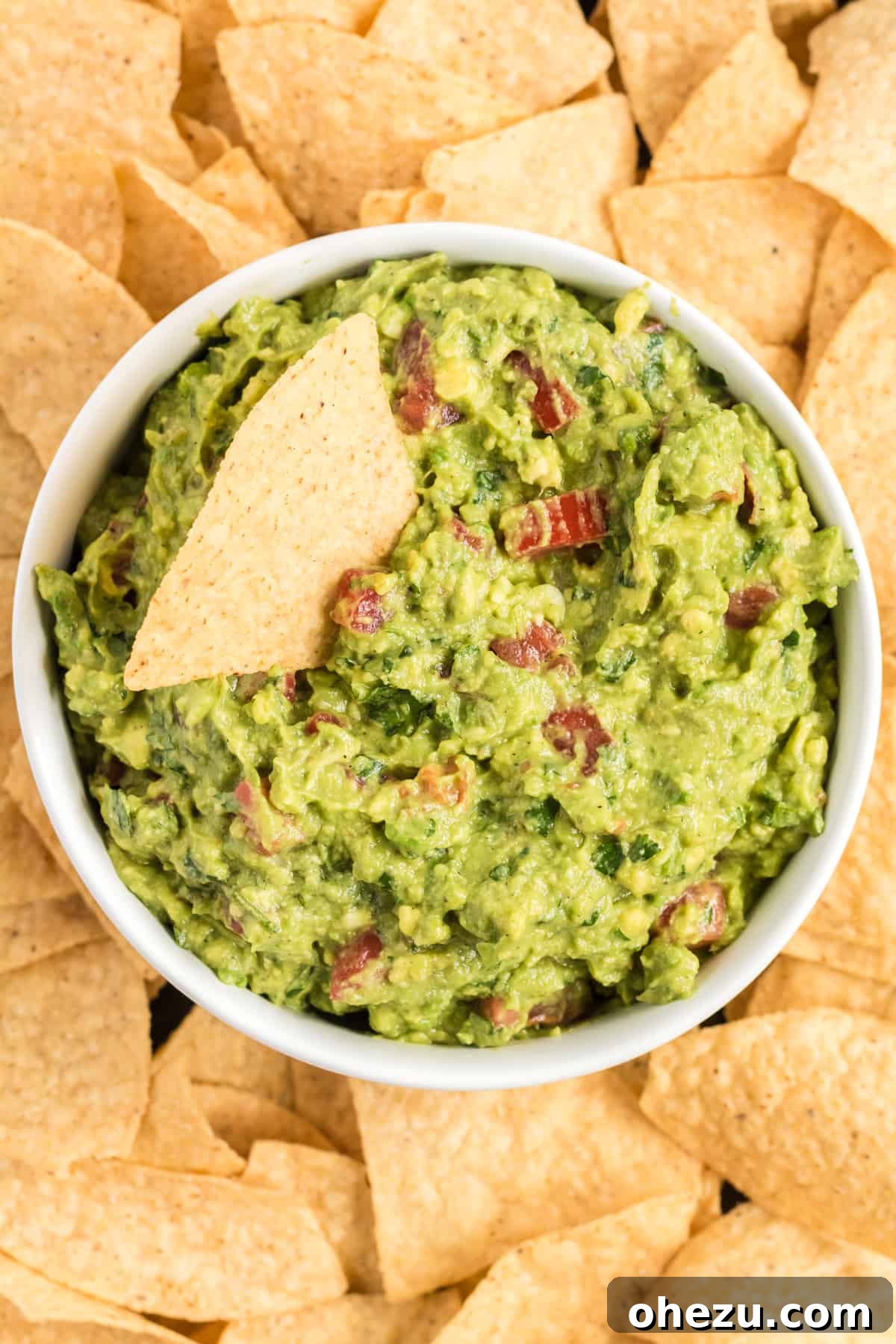 A rustic bowl filled with chunky, fresh guacamole, surrounded by crispy tortilla chips on a wooden platter.