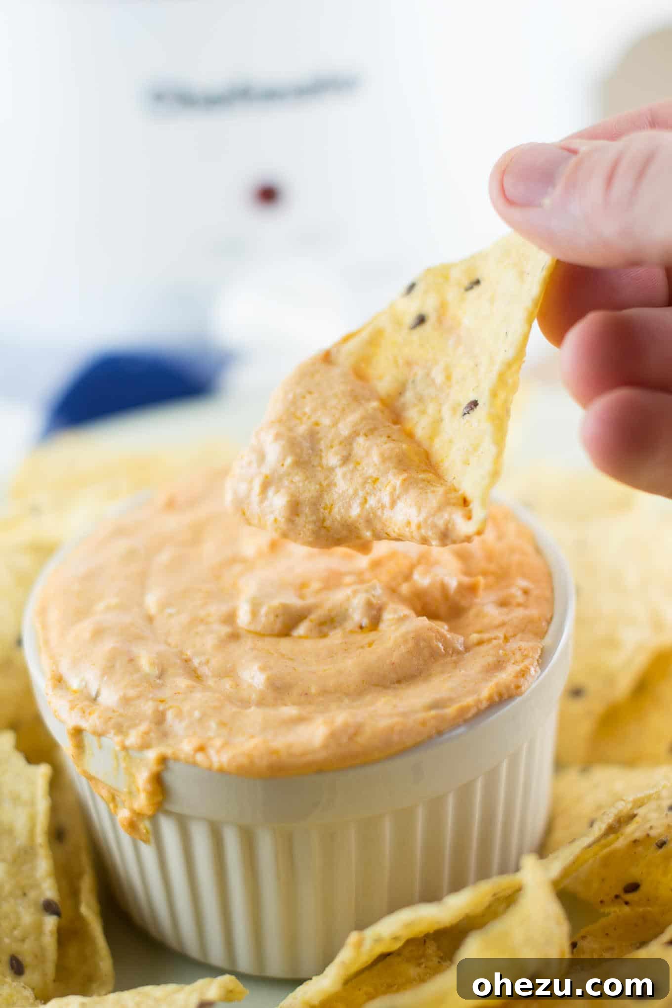 A bubbling, creamy queso dip in a slow cooker, with a serving spoon and tortilla chips nearby, perfect for a party.