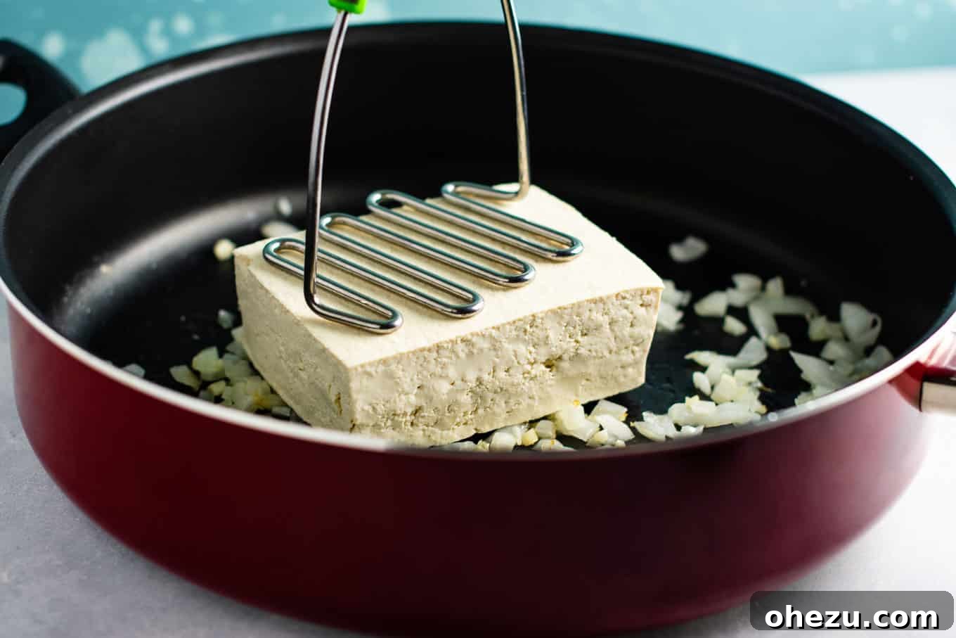 Mashing extra firm tofu in a skillet to achieve egg-like texture for an easy #tofuscramble recipe. Perfect for #veganbreakfast.
