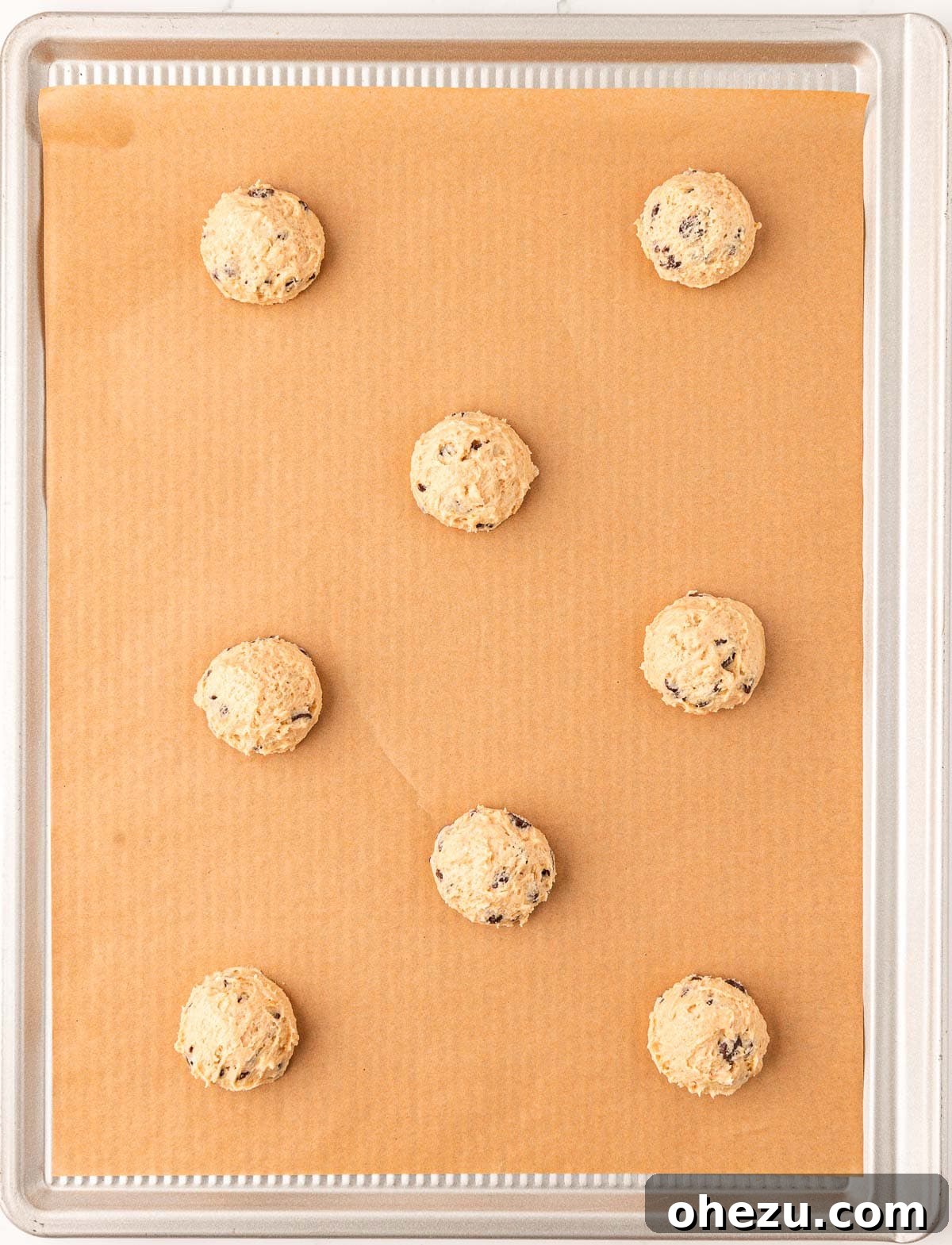 Heavenly Vegan Chocolate Chip Cookies 13 Scooped portions of vegan chocolate chip cookie dough evenly spaced on a parchment-lined baking sheet, ready for baking.