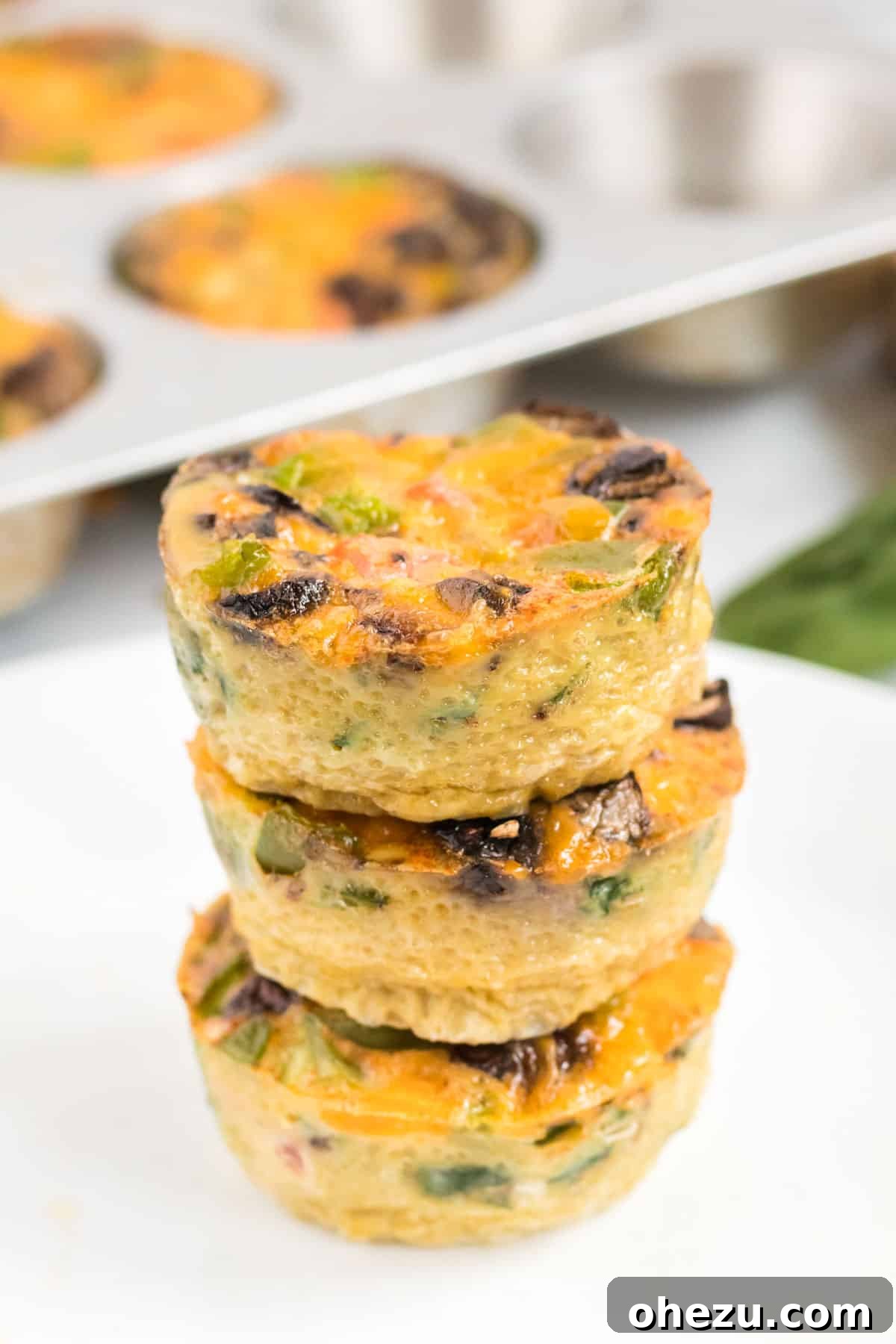 A stack of perfectly cooked egg muffins, showcasing their golden-brown tops and colorful veggie fillings.