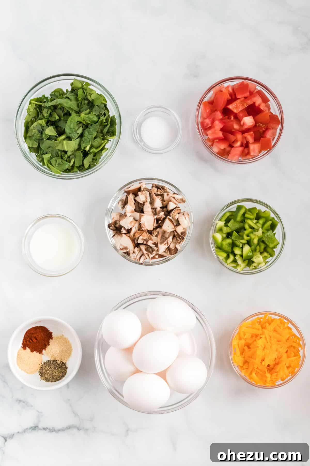 A vibrant display of fresh ingredients, including eggs, spinach, tomatoes, mushrooms, bell peppers, milk, and cheese, laid out for making egg muffin cups.