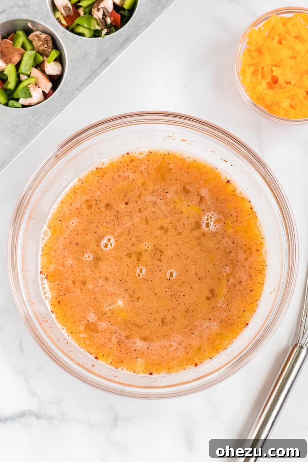 A glass bowl filled with a perfectly whisked egg batter, seasoned and ready for pouring into the muffin tin.