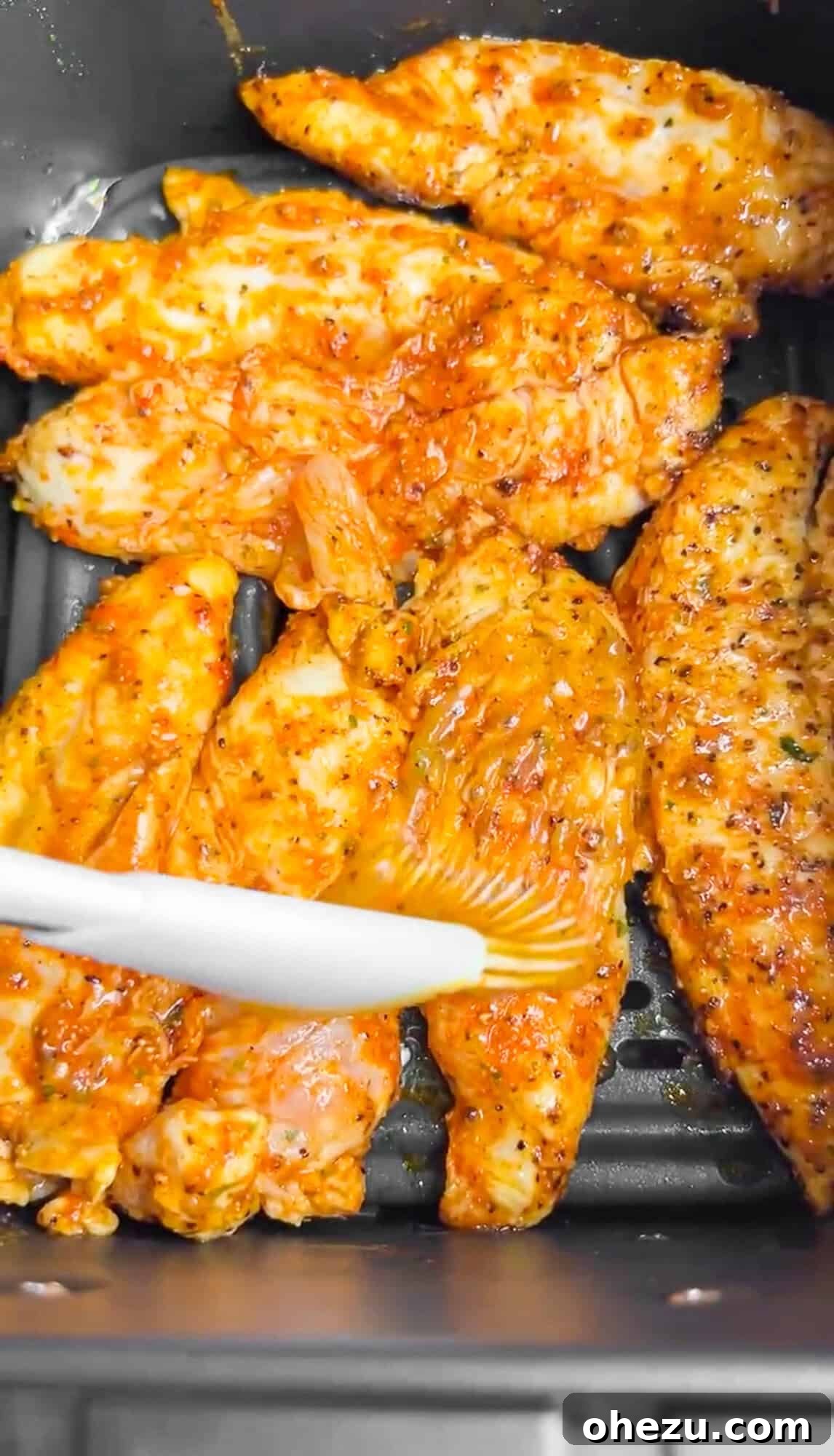 Air-Fried Hot Lemon Pepper Ranch Chicken Tenders 7 A hand using a basting brush to apply glaze to chicken tenders inside an air fryer basket.