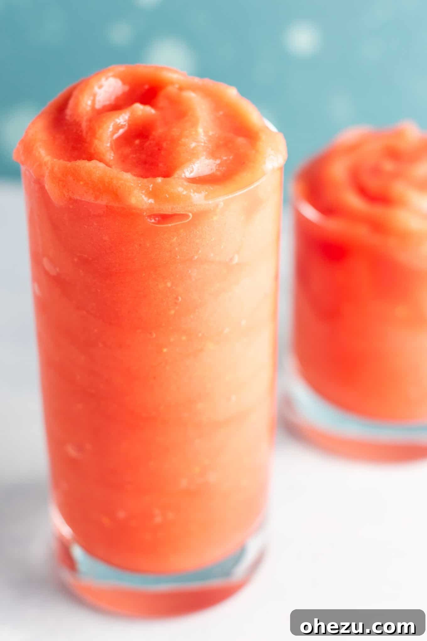 A hand holding a glass of watermelon gin slushie against a bright summer background.