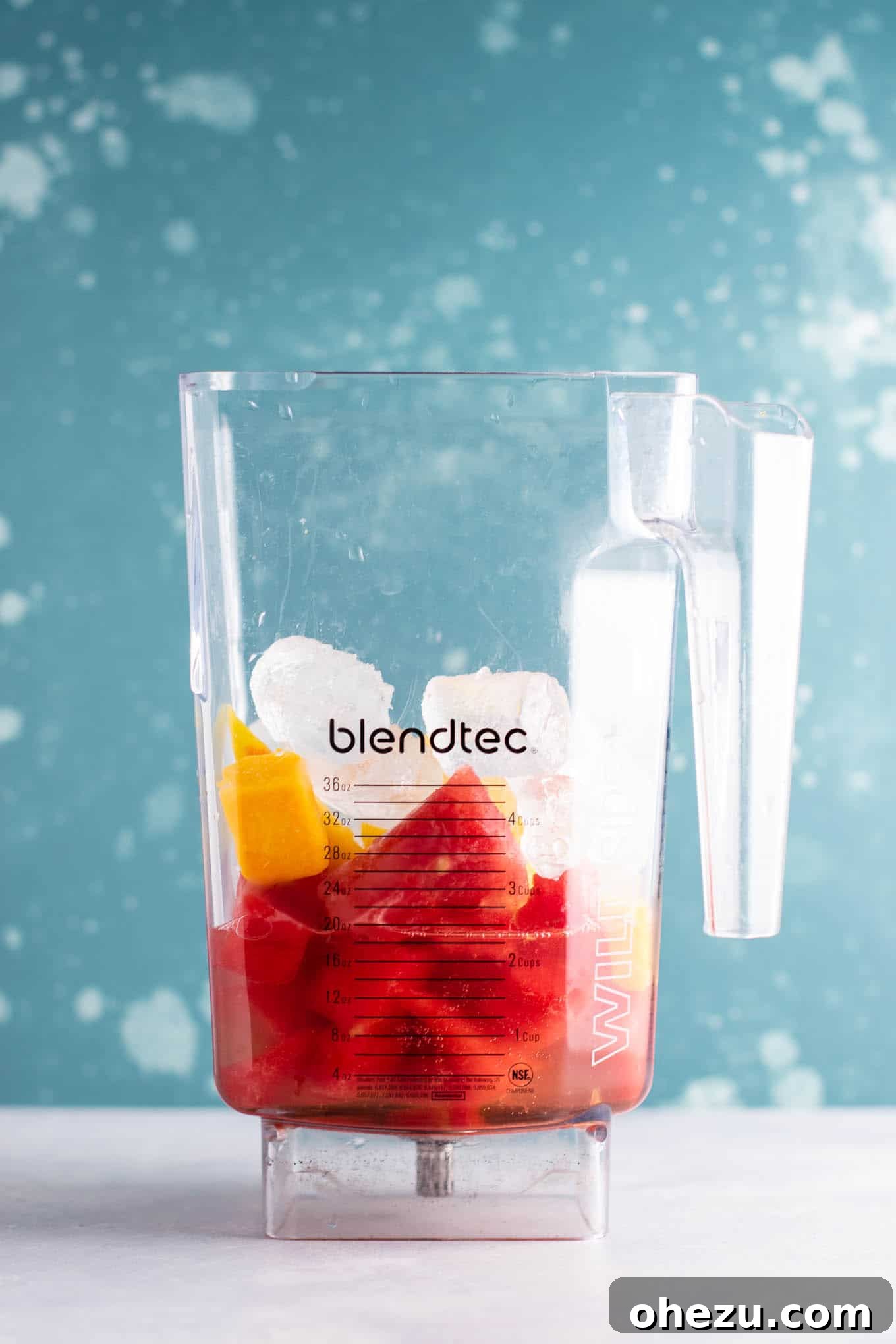 Fresh watermelon chunks, mango, peaches, and gin on a countertop, ready for blending.