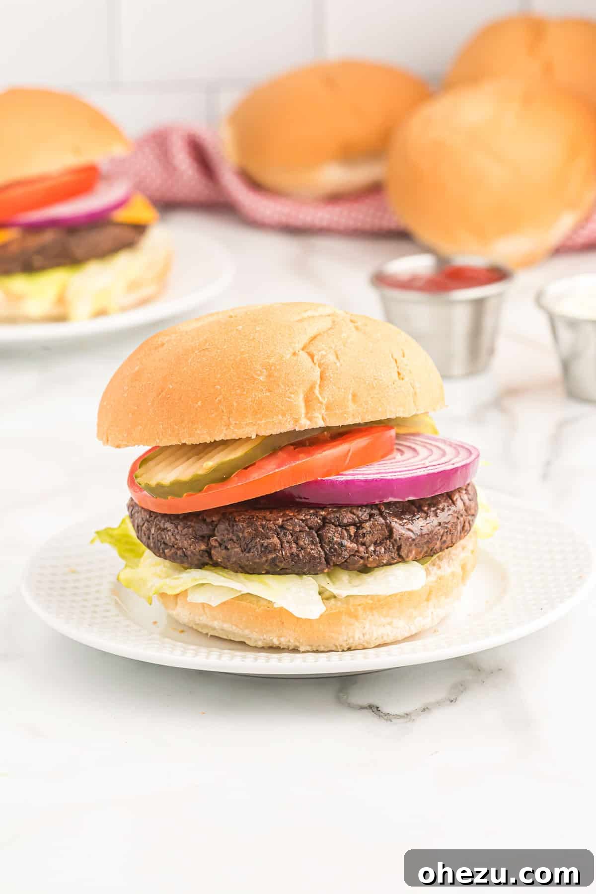 A black bean burger on a brioche bun, generously topped with fresh pickles, ripe tomato, crisp lettuce, and thinly sliced red onion.