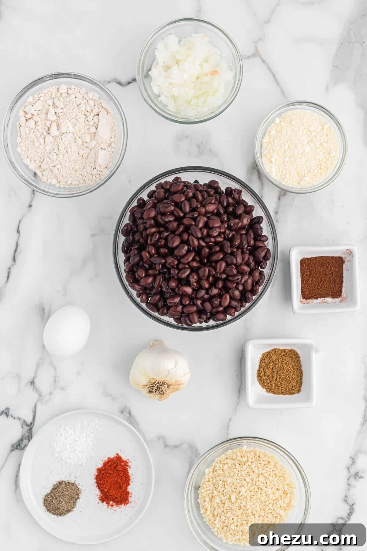 An array of fresh ingredients laid out, including black beans, onion, garlic, eggs, and various spices, ready for making homemade black bean burgers.