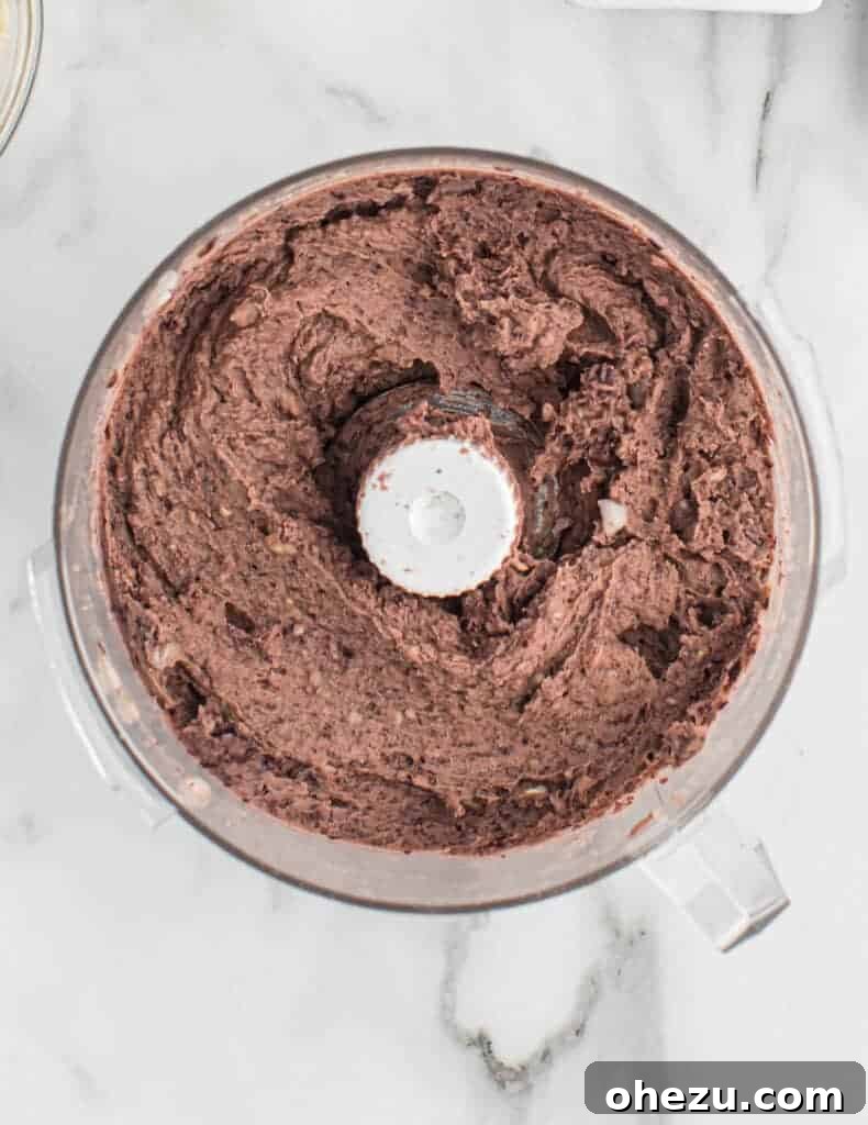 Smooth, well-combined black bean burger batter in a food processor, resembling refried beans.
