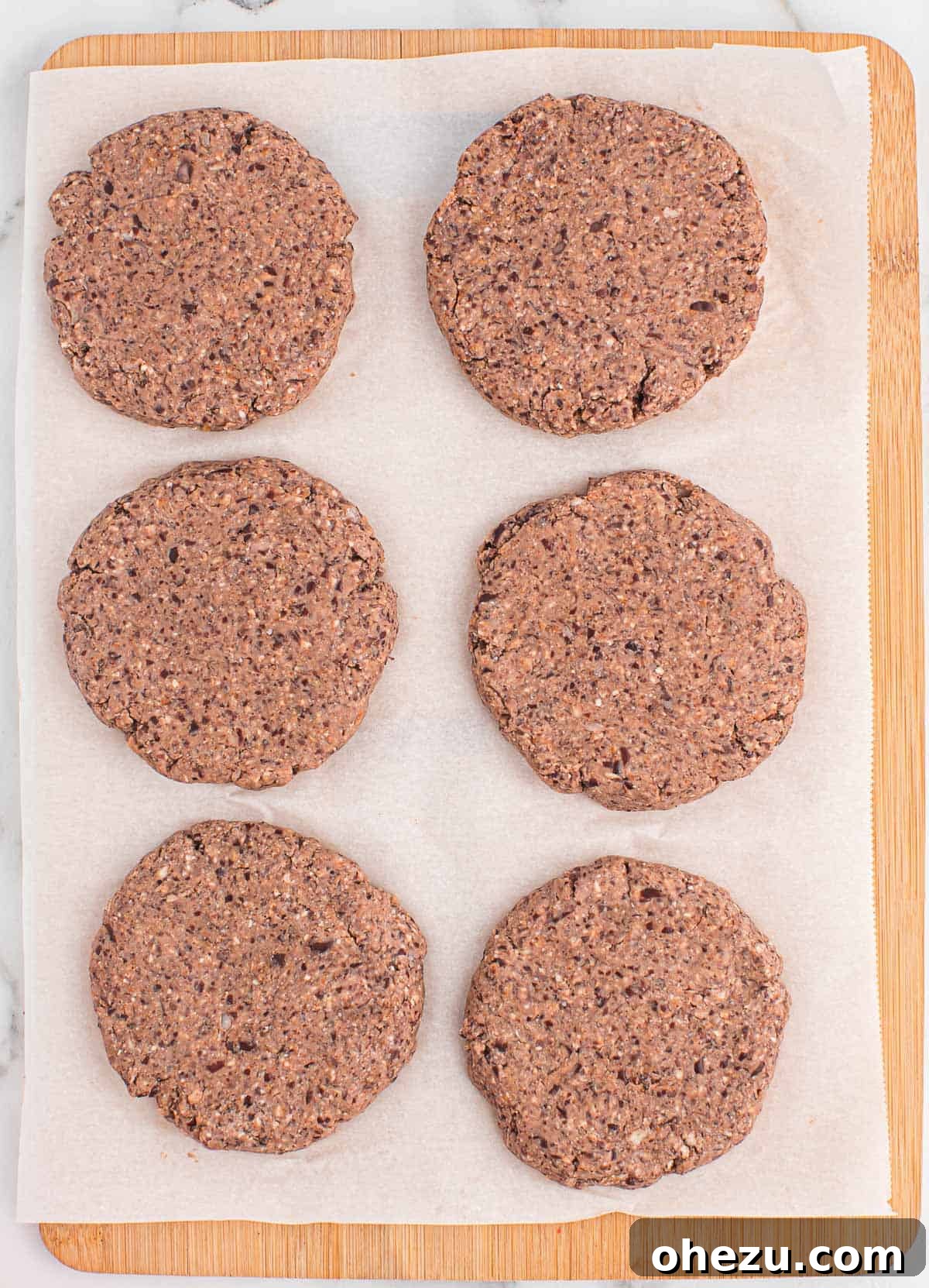 Six perfectly shaped black bean burger patties resting on parchment paper, ready to be cooked.