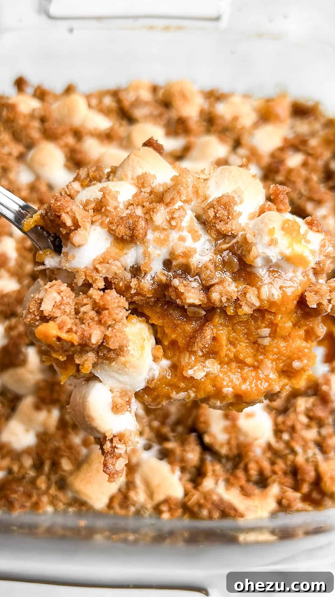 A serving spoon scoops out a portion of Southern Sweet Potato Casserole, showcasing its creamy texture and layered toppings.