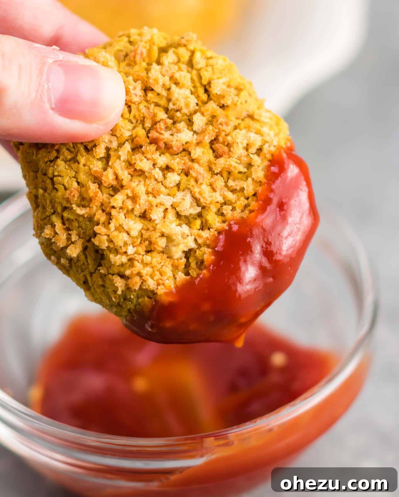 Golden Chickpea Bites 7 A golden-brown vegetarian chickpea nugget being dipped into a swirl of red ketchup, ready for a flavorful bite.