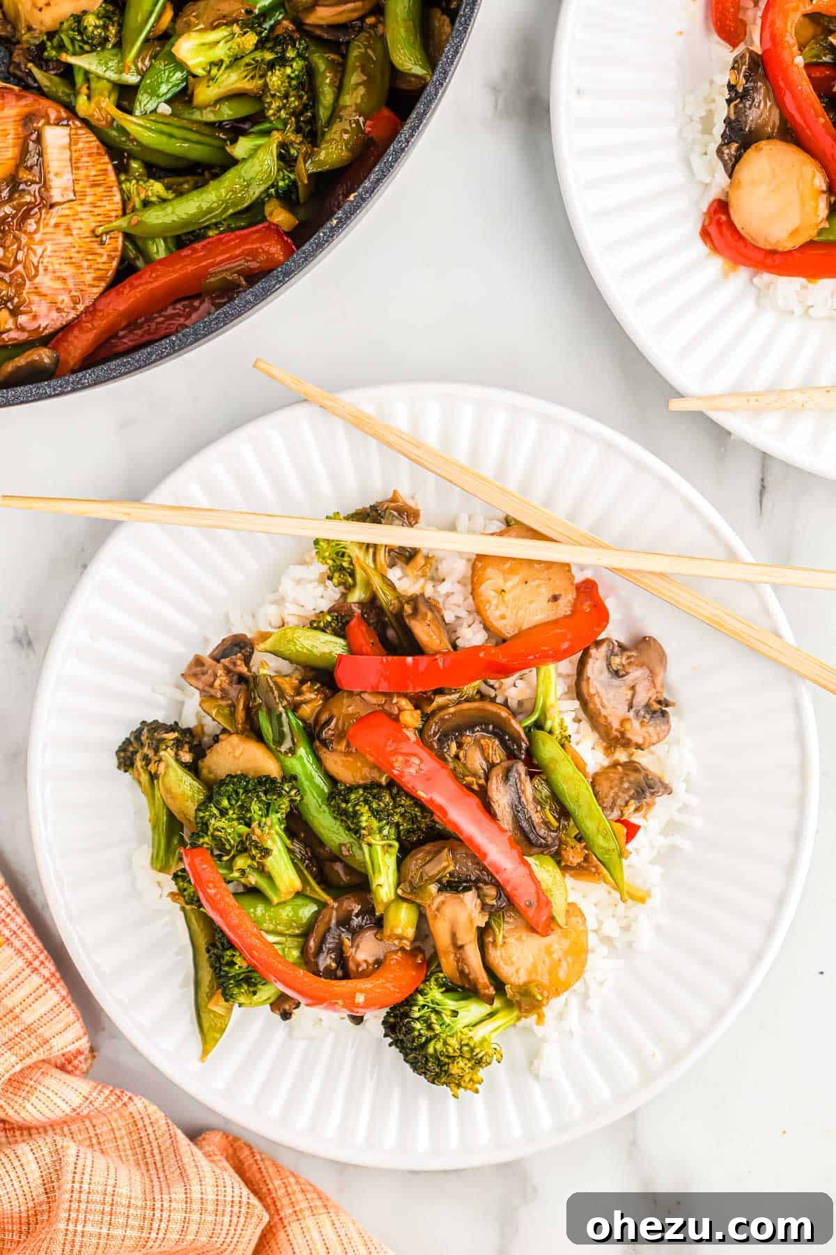 veggie stir fry over white rice on a plate with chopsticks