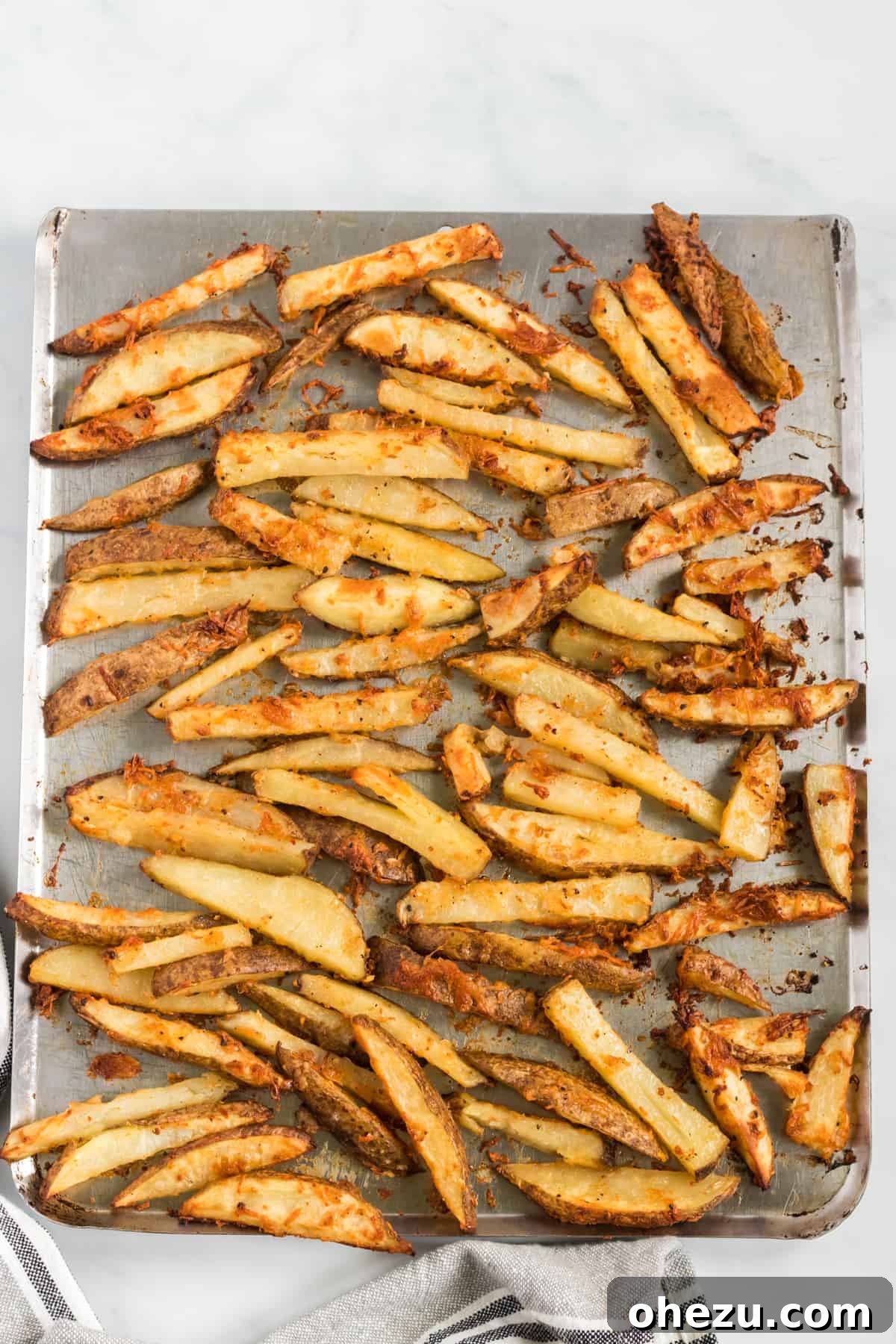 Crispy parmesan potato wedges spread evenly on a baking sheet, fresh out of the oven.