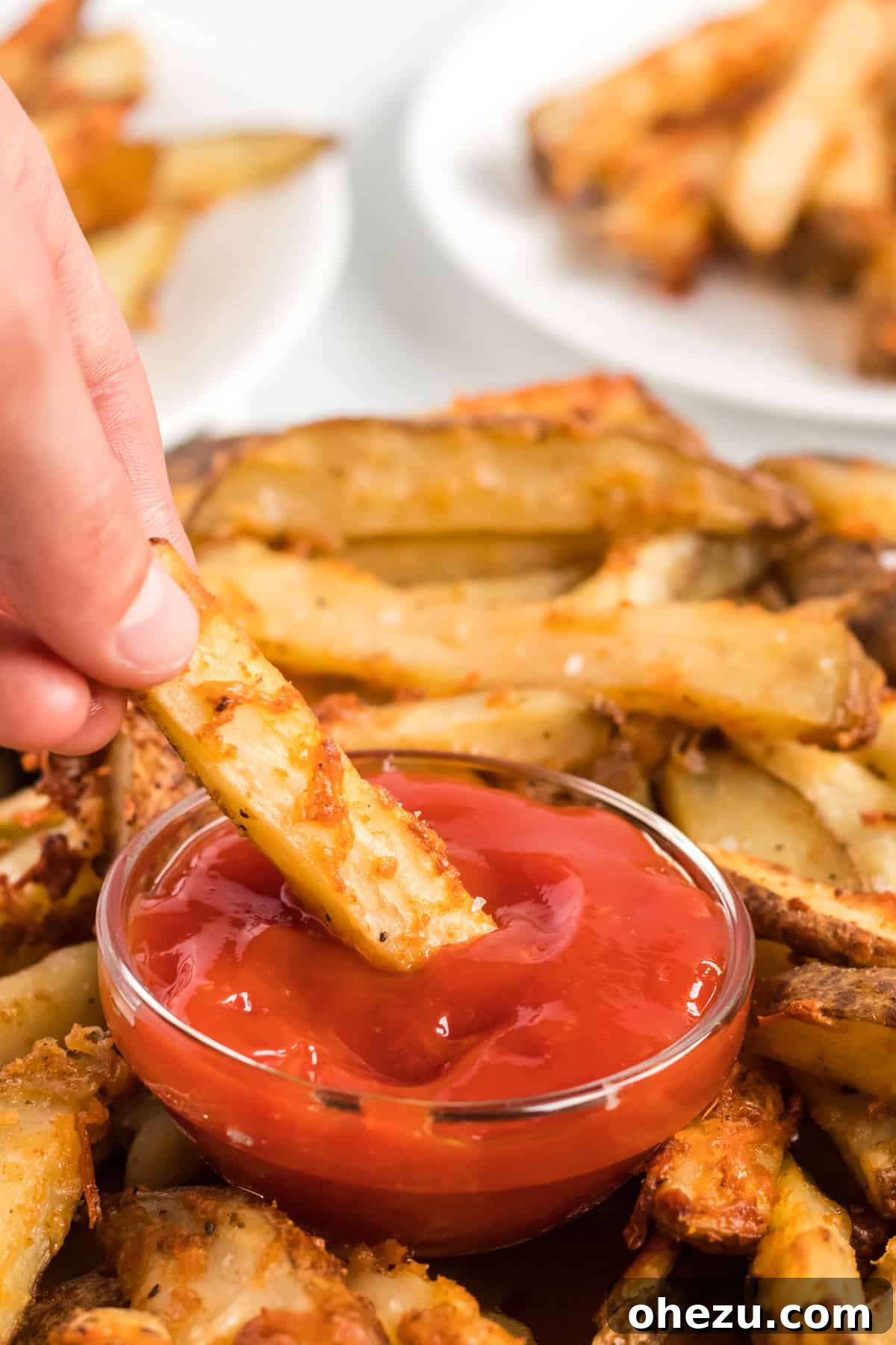 A parmesan crusted potato wedge being dipped into a small bowl of ketchup, highlighting its crispy texture.