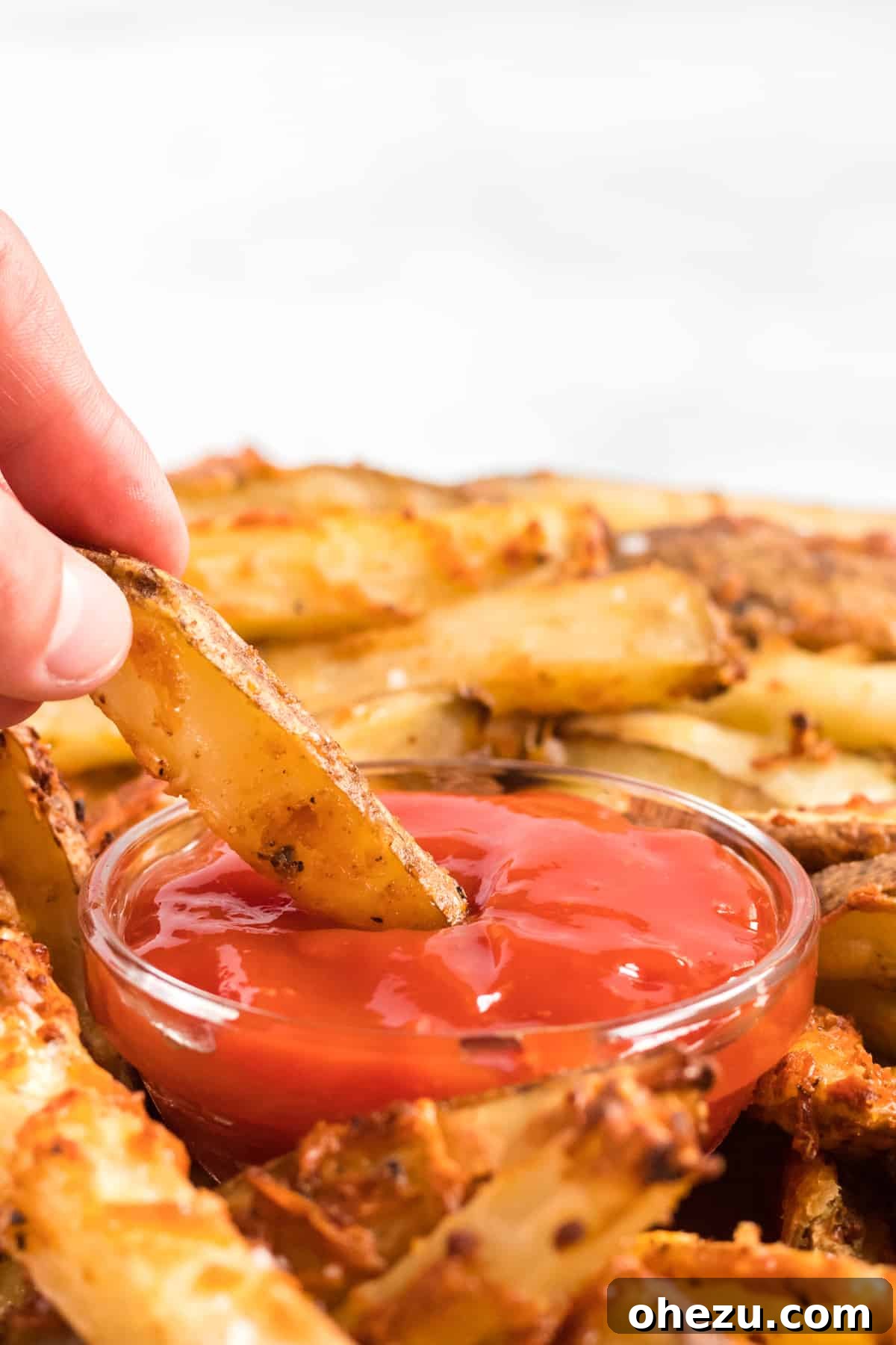 Another close-up of a parmesan crusted potato wedge being dipped in ketchup, emphasizing the rich flavor and texture.